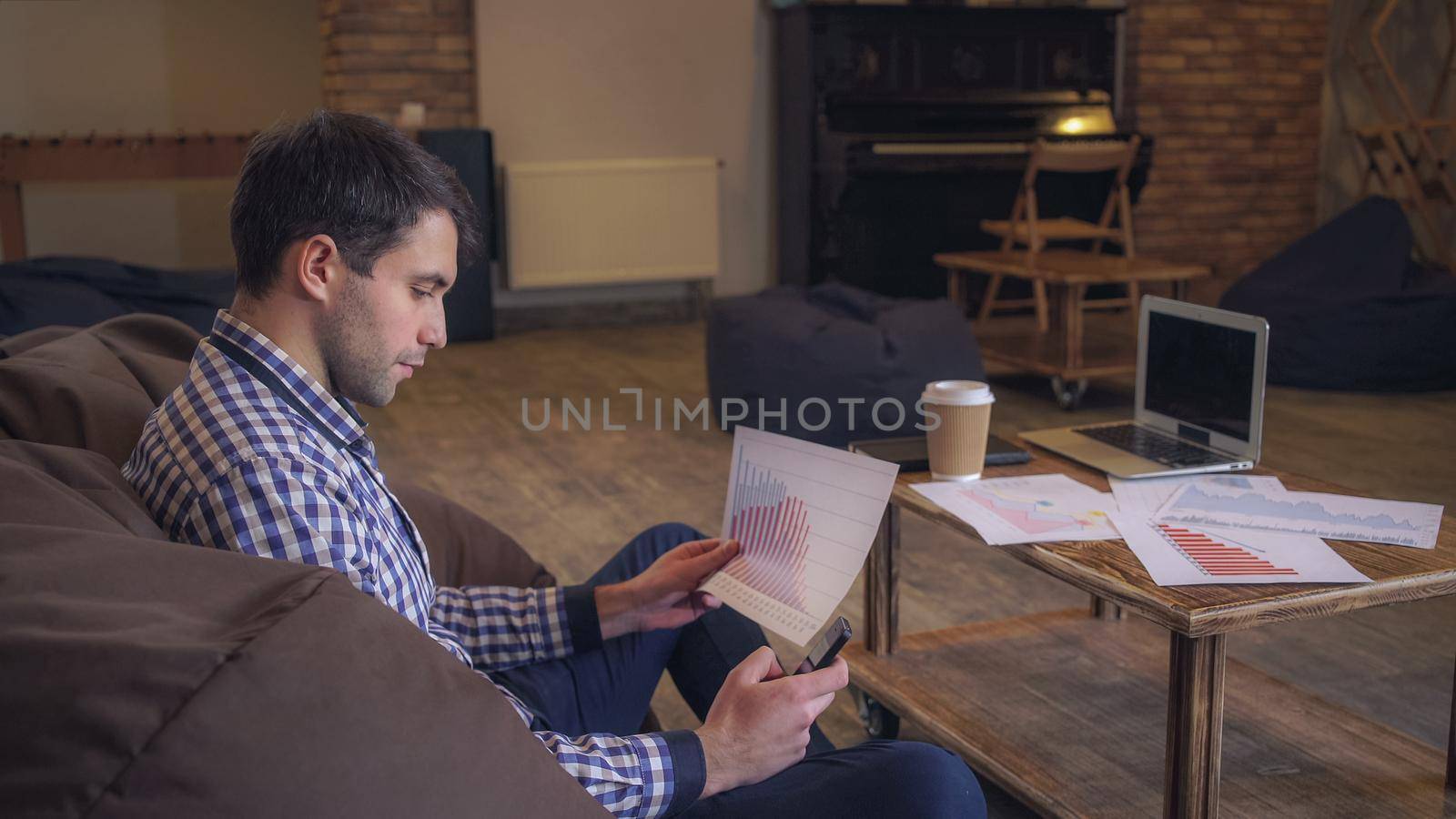 Manager working in coworking, in the hands holding the phone checks the data raspechatonym document on the table laptop and diary.