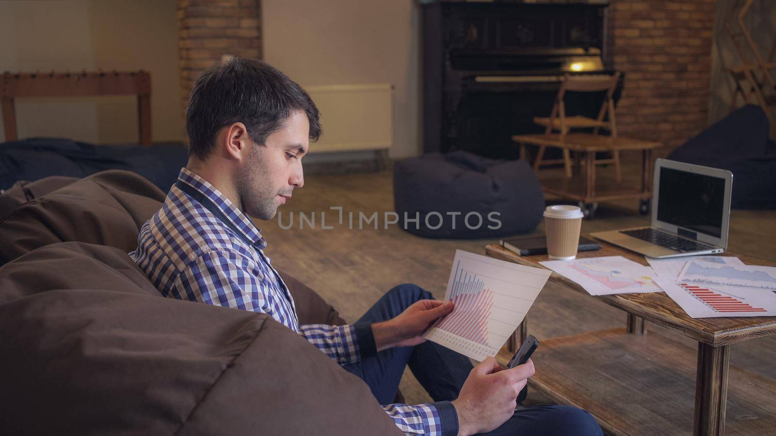 Manager working in coworking, in the hands holding the phone checks the data raspechatonym document on the table laptop and diary.