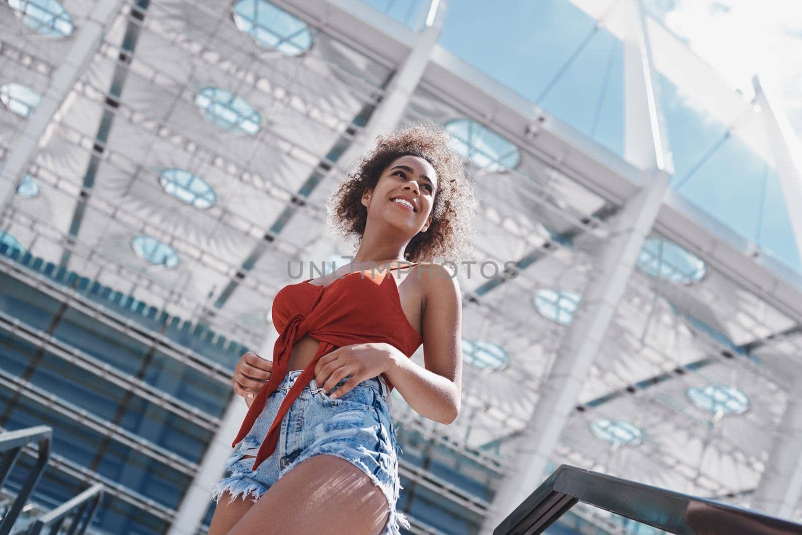 Young woman wearing top and jeans shorts free style on the street walking down the concrete stairs looking aside smiling dreamful bottom view