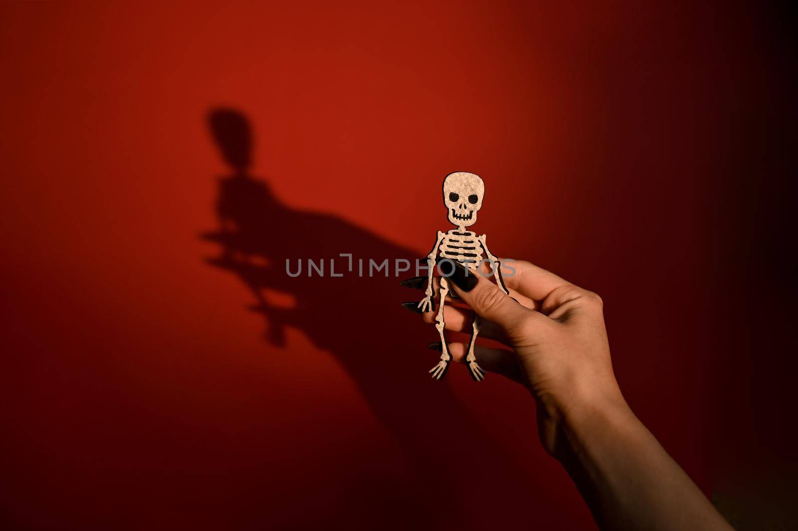 Postcard for Halloween. a human skeleton toy in hand with a shadow on a red background. Halloween symbol. copy space.