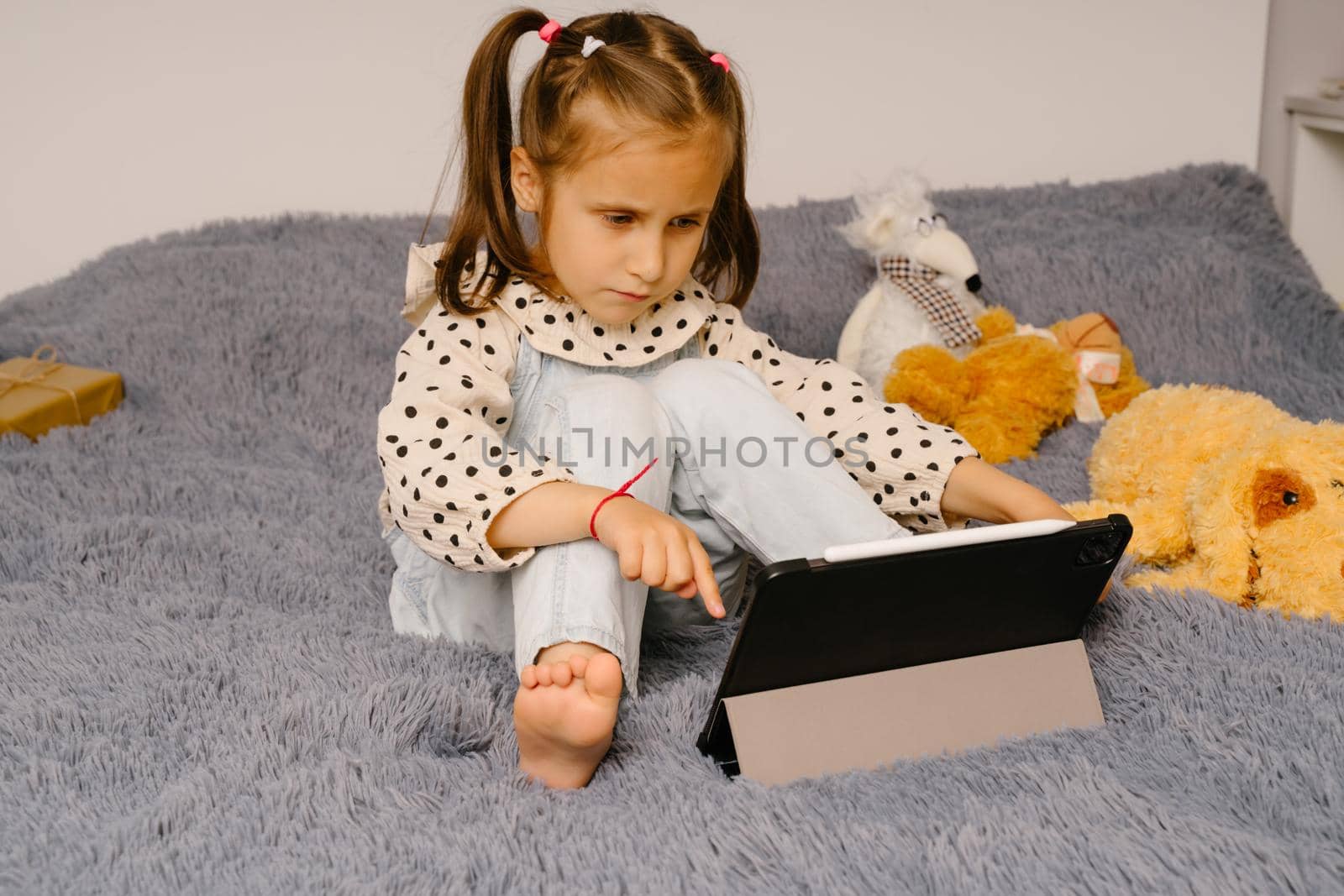 A girl is talking very emotionally over a video link. The girl sits on the bed and watches cartoons or lessons. Distance learning via video communication. Modern technologies in training.