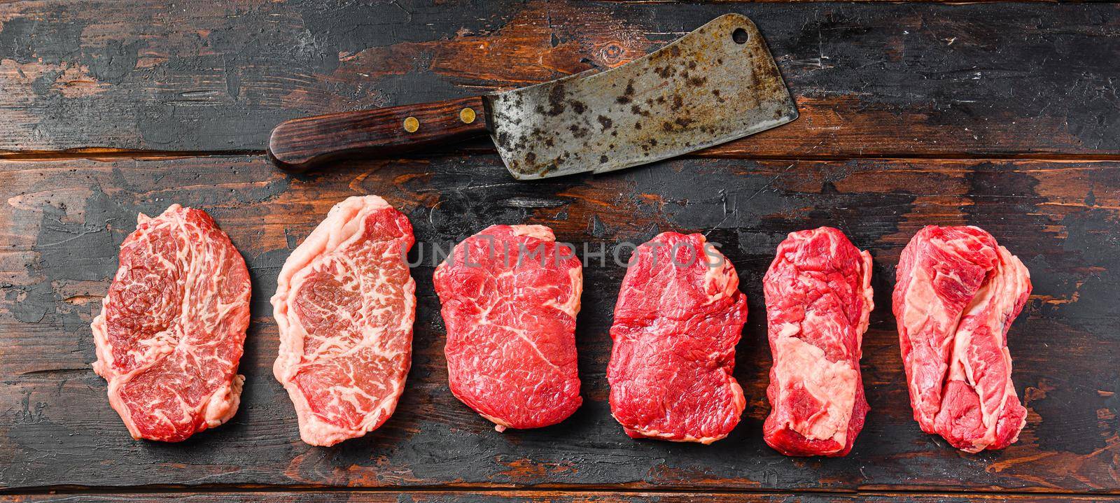 A set of different types of raw beef steaks:top blade, rump, chuck eye roll over old wooden background top view with butcher cleaver. by Ilianesolenyi