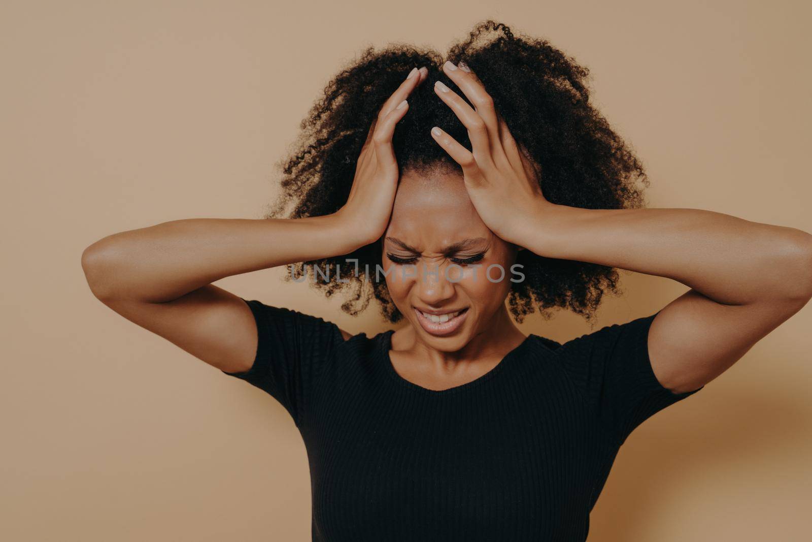 Studio shot of stressful and frustrated young african woman keeping head with both hands with closed eyes, displeased female suffering from headache or having problems at work. Stress and depression