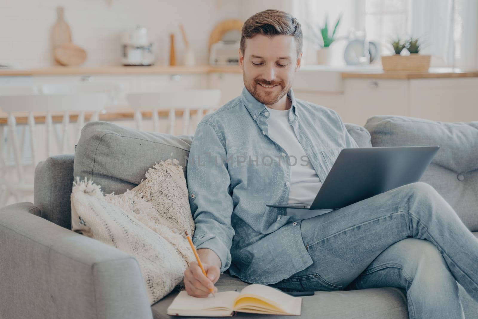 Young office worker working remotely from home researching using notebook and taking notes by vkstock