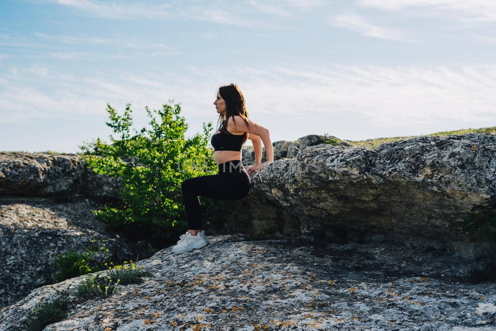 A girl in a black suit and white sneakers is engaged in sports in the mountains. Outdoor sports. The girl performs a sports exercise.