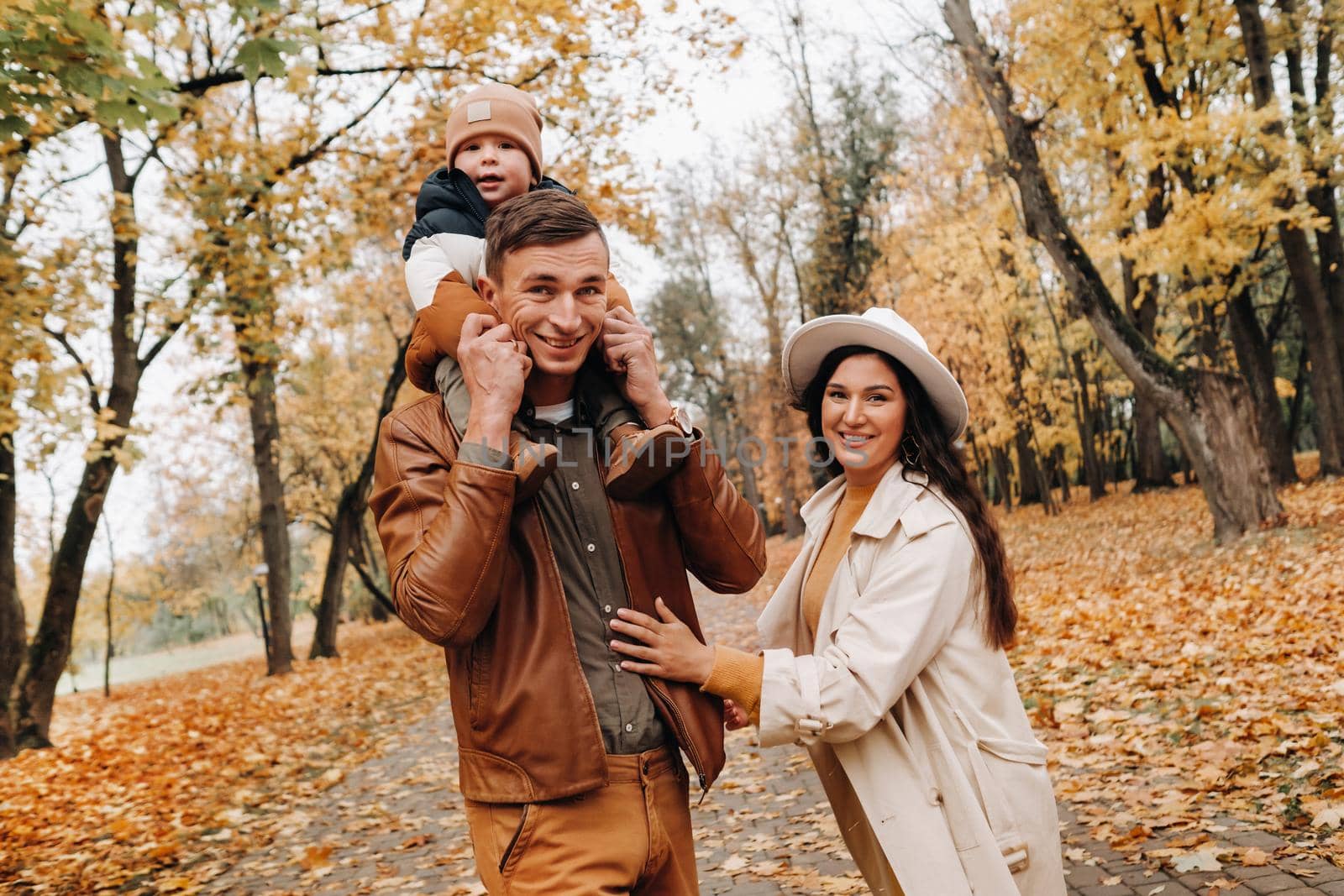 Father and mother with son walking in the autumn Park. A family walks in the Golden autumn in a nature Park. by Lobachad