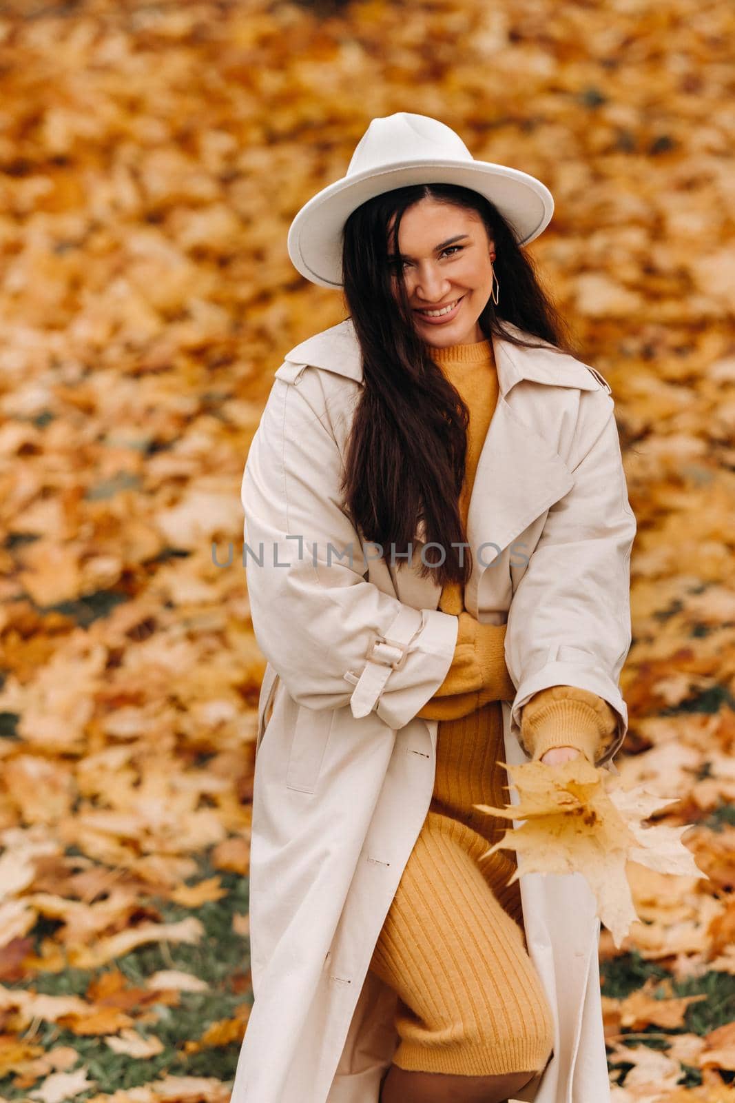 a cheerful girl in a white coat and hat smiles in an autumn Park.portrait of a smiling woman in Golden autumn