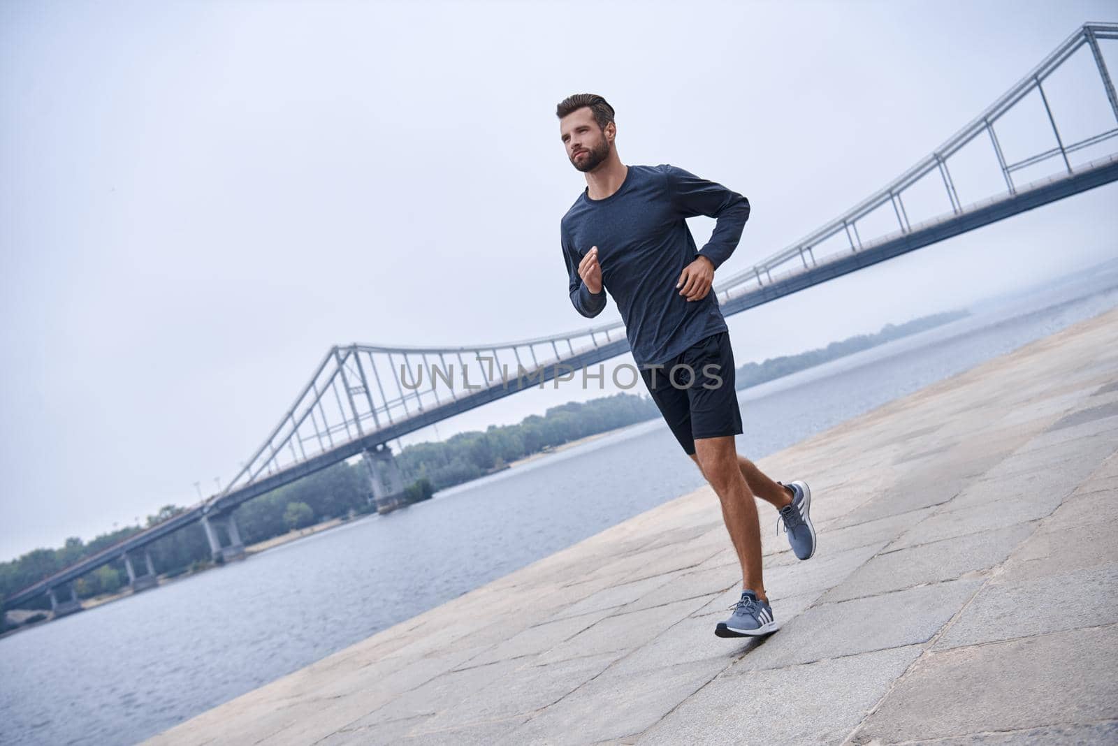 Morning workout. Full length rear view of young man in sports clothing exercising while jogging on the bridge outdoors by friendsstock