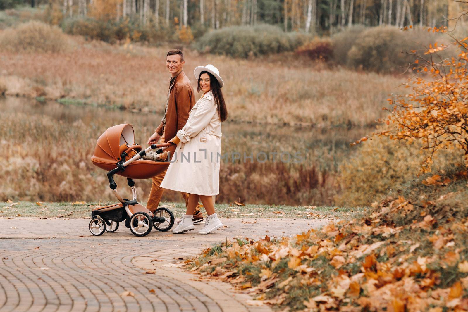 Father and mother on a walk with a stroller in the autumn Park. The family walks through the nature Park in the Golden autumn