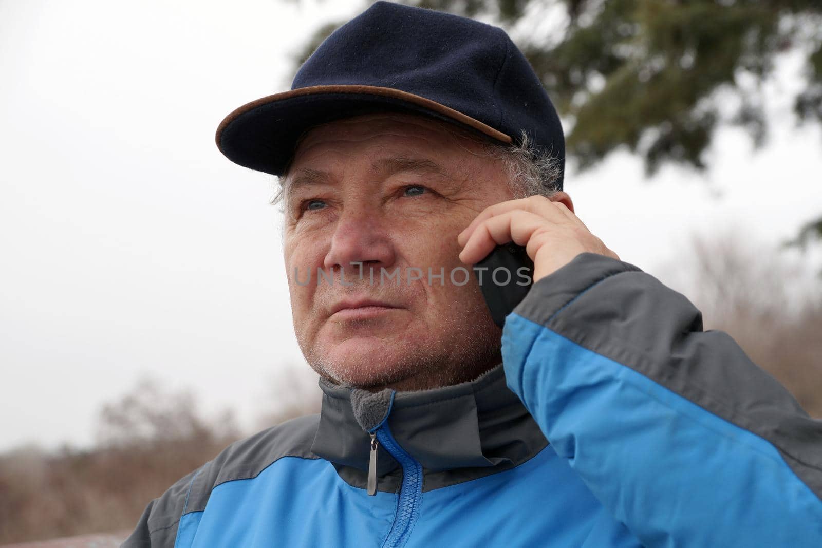 portrait of a middle-aged man talking on the phone in a cap on a natural background by Annado