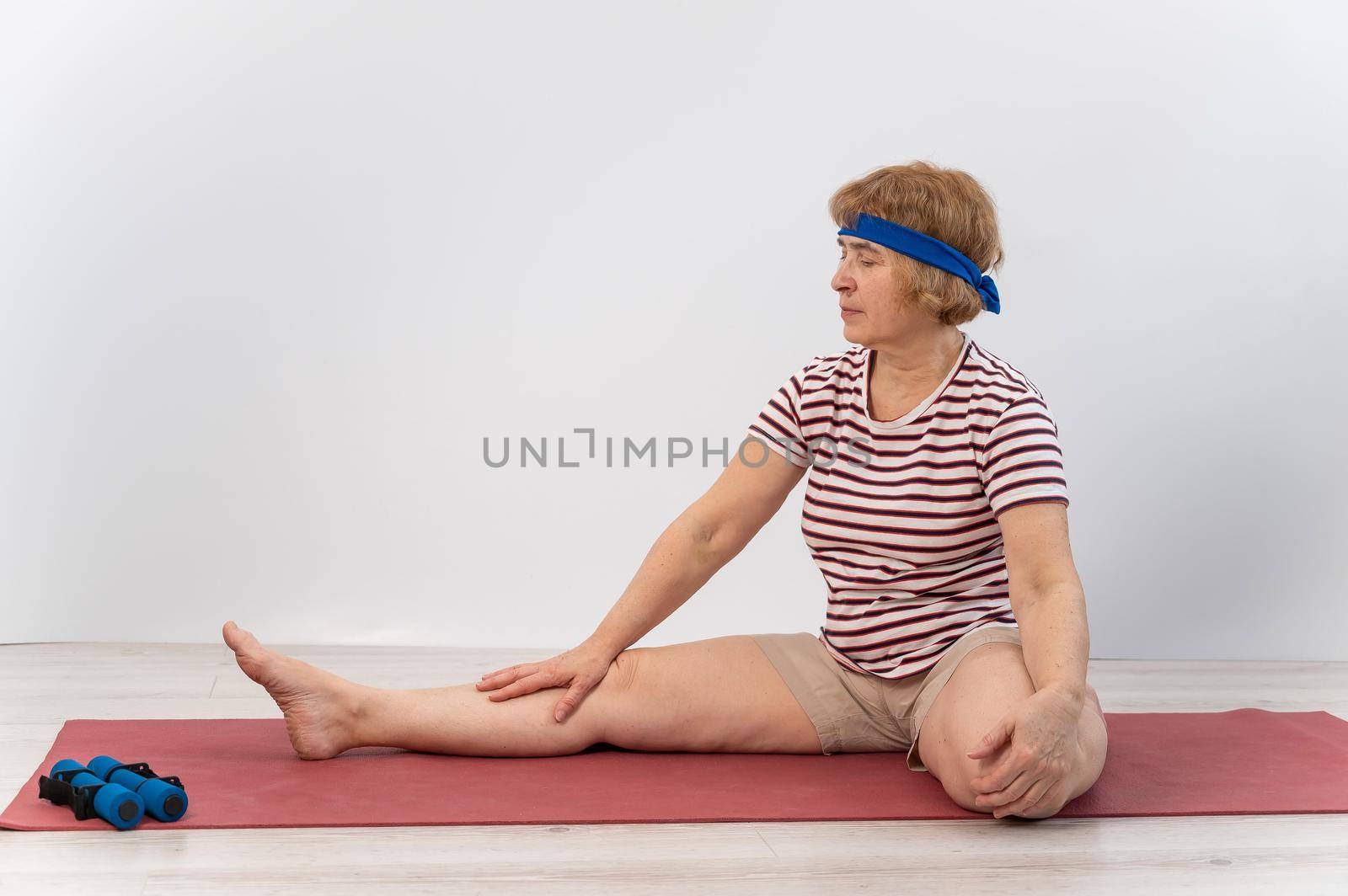 Elderly woman makes bends on a white background. Old lady doing health stretching exercises by mrwed54
