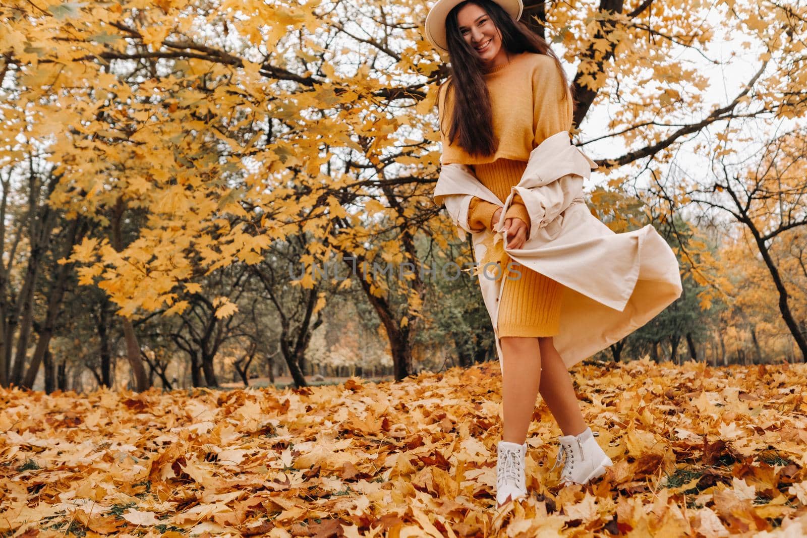 a cheerful girl in a white coat and hat smiles in an autumn Park.portrait of a smiling woman in Golden autumn. by Lobachad