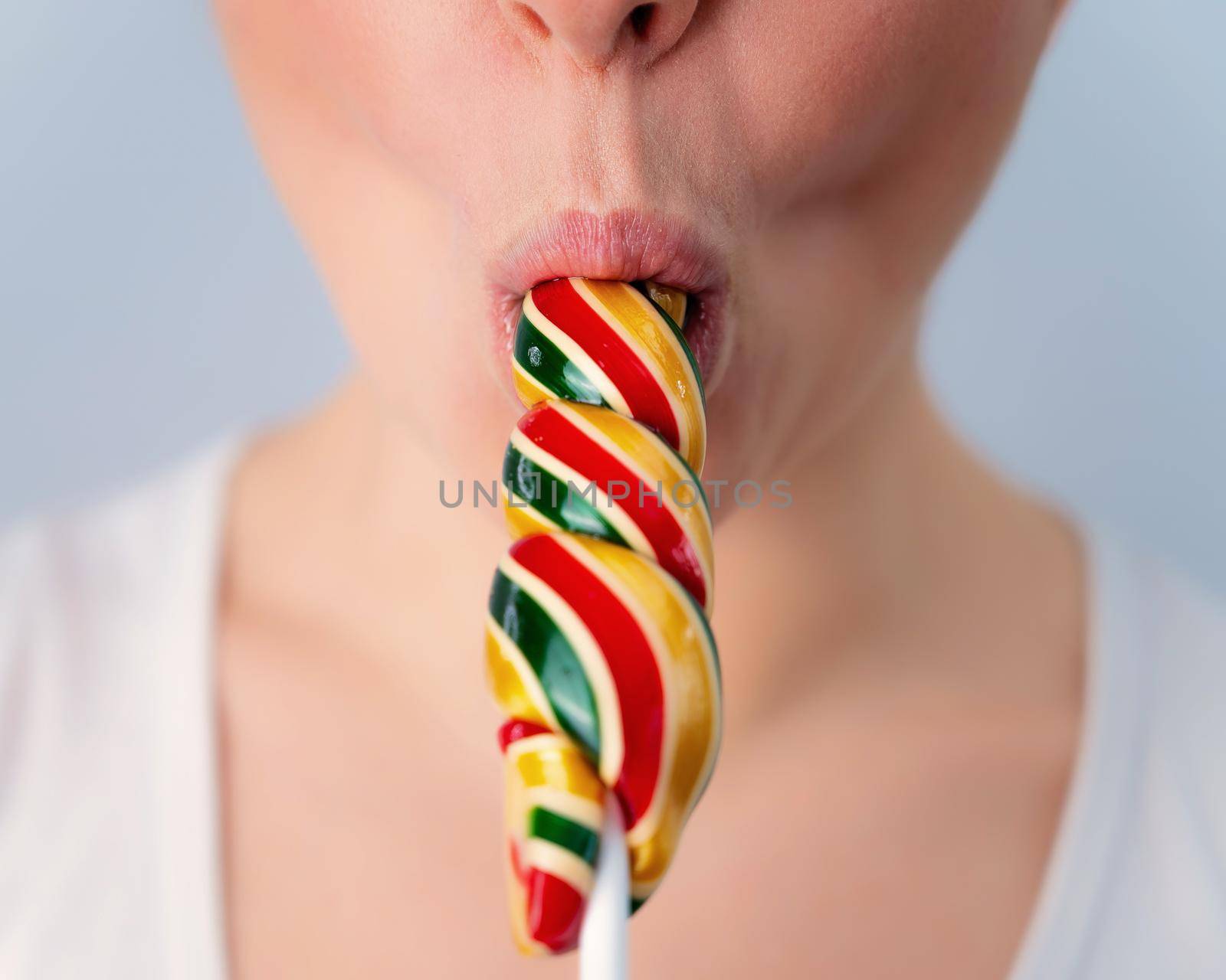 Close-up portrait of a woman sucking a long lollipop against a white background. Blowjob simulation.