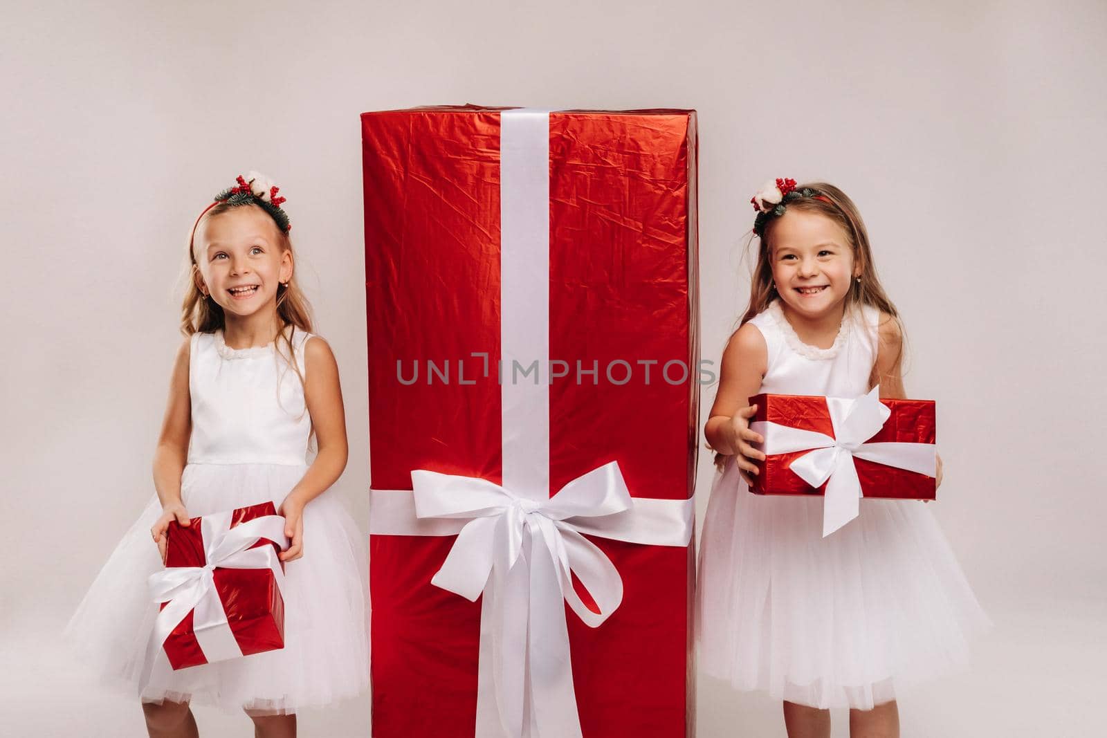 two little girls with Christmas gifts on a white background and a huge gift.