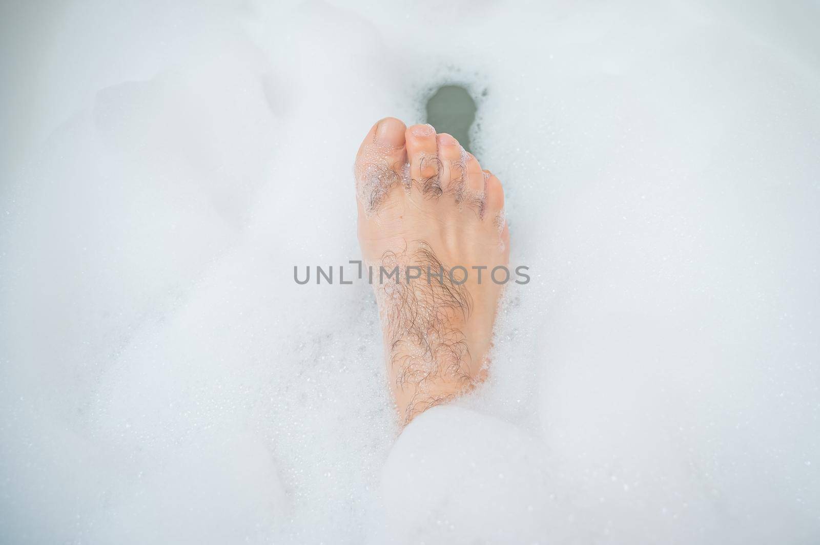 Funny picture of a man taking a relaxing bath. Close-up of male feet in a bubble bath.