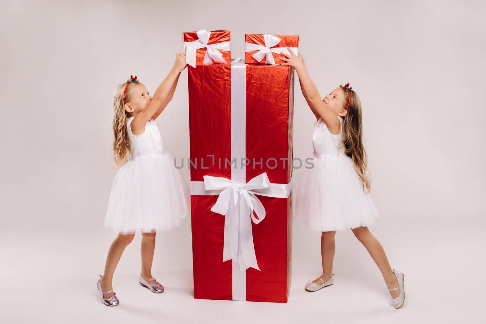 two little girls with Christmas gifts on a white background and a huge gift.