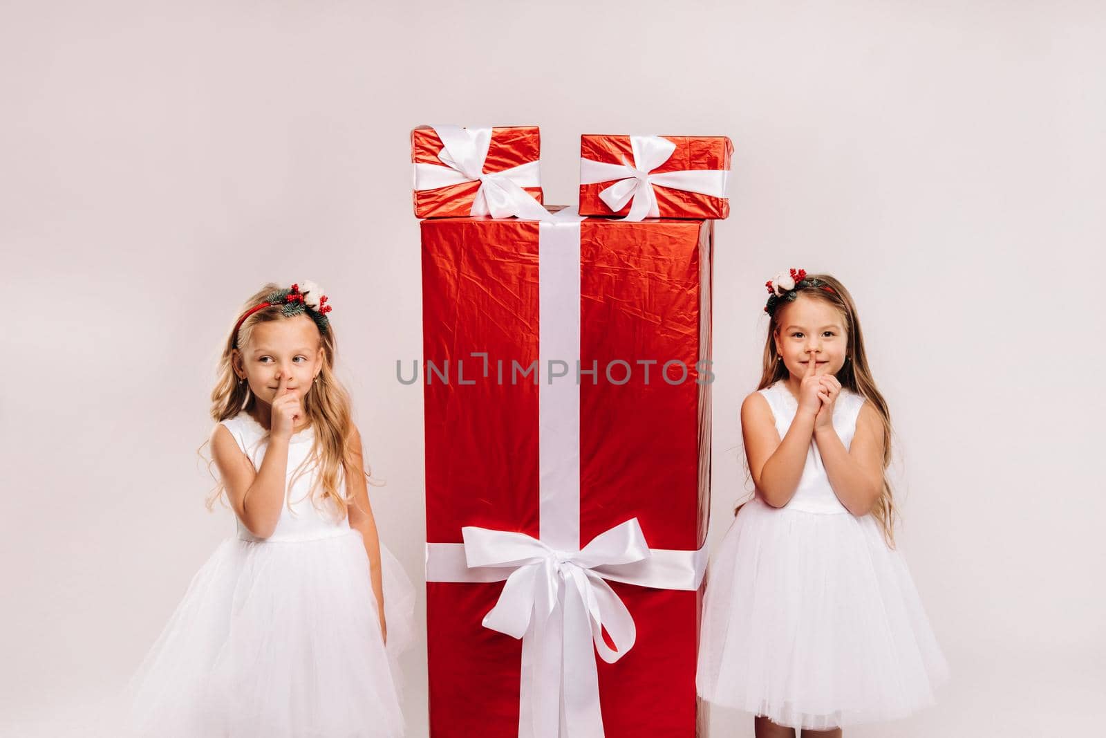 two little girls with Christmas gifts on a white background and a huge gift.