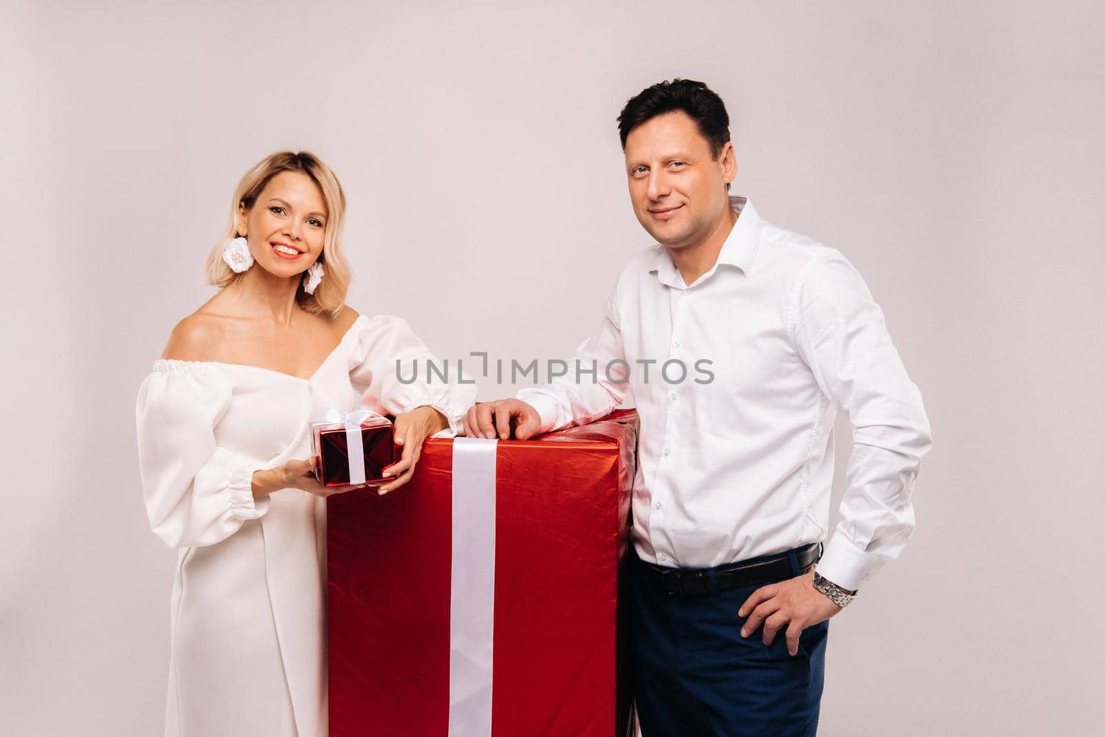 Portrait of a man and a woman with a large gift on a beige background.