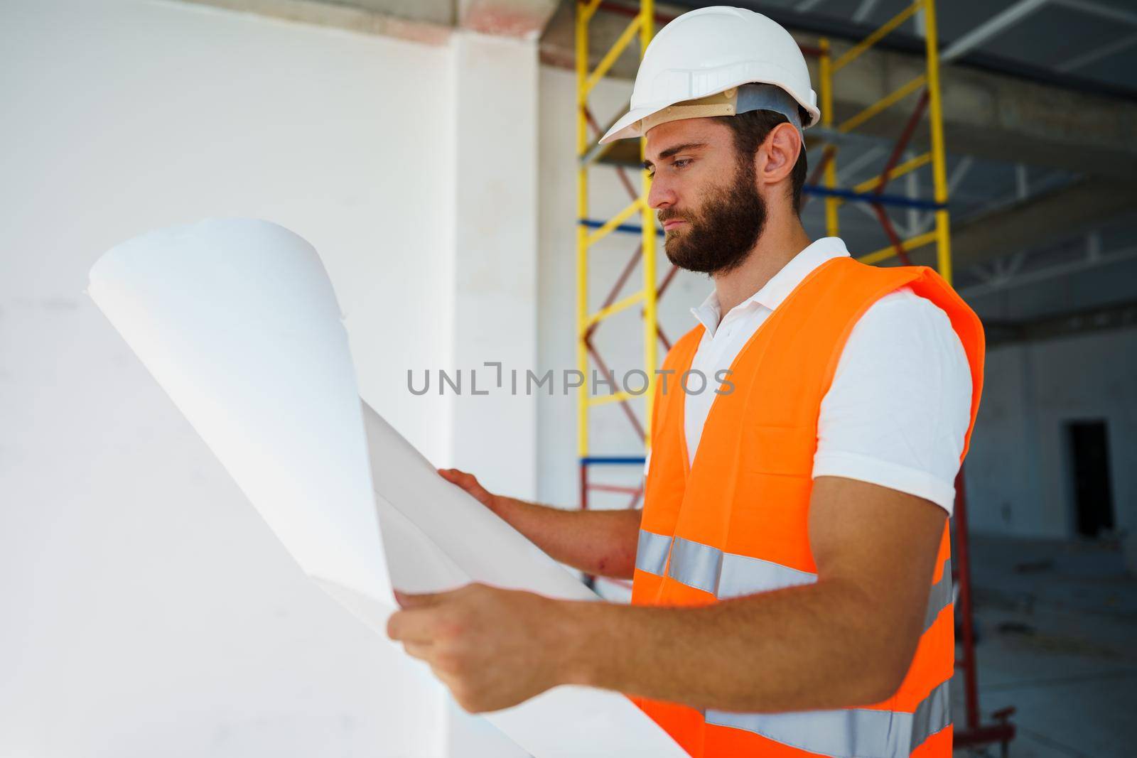 Builder or architect in hardhat supervising a project, looking at blueprints, close up