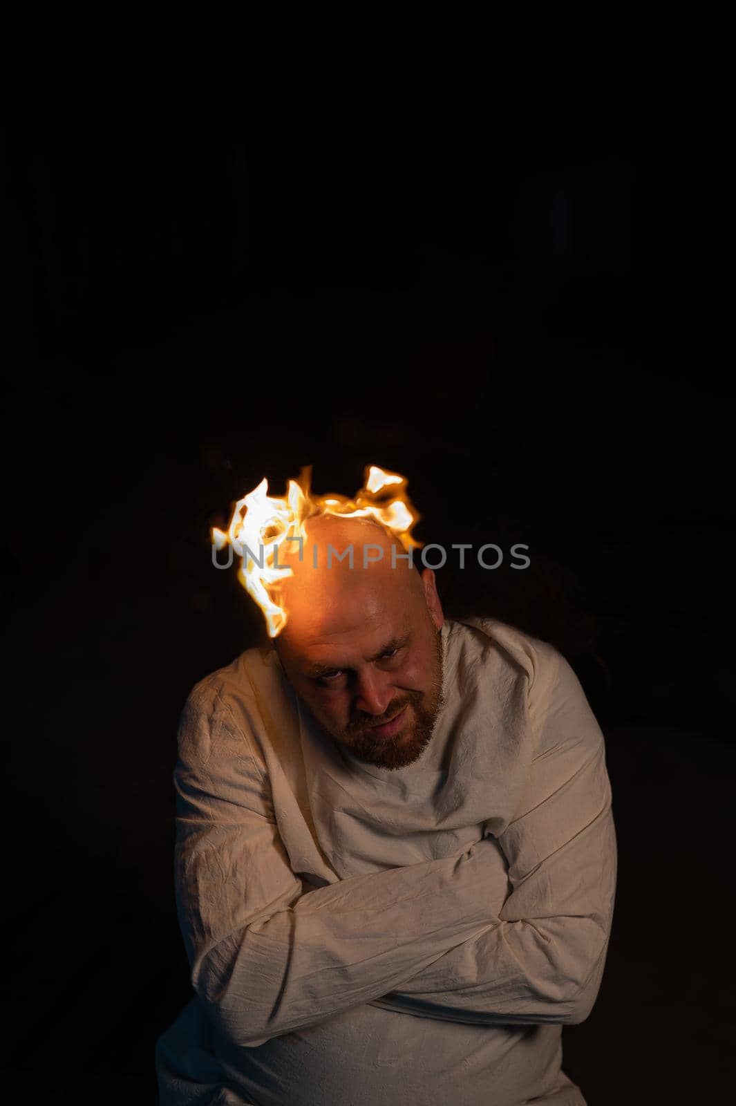 Bald man in a straitjacket with a burning head on a dark background