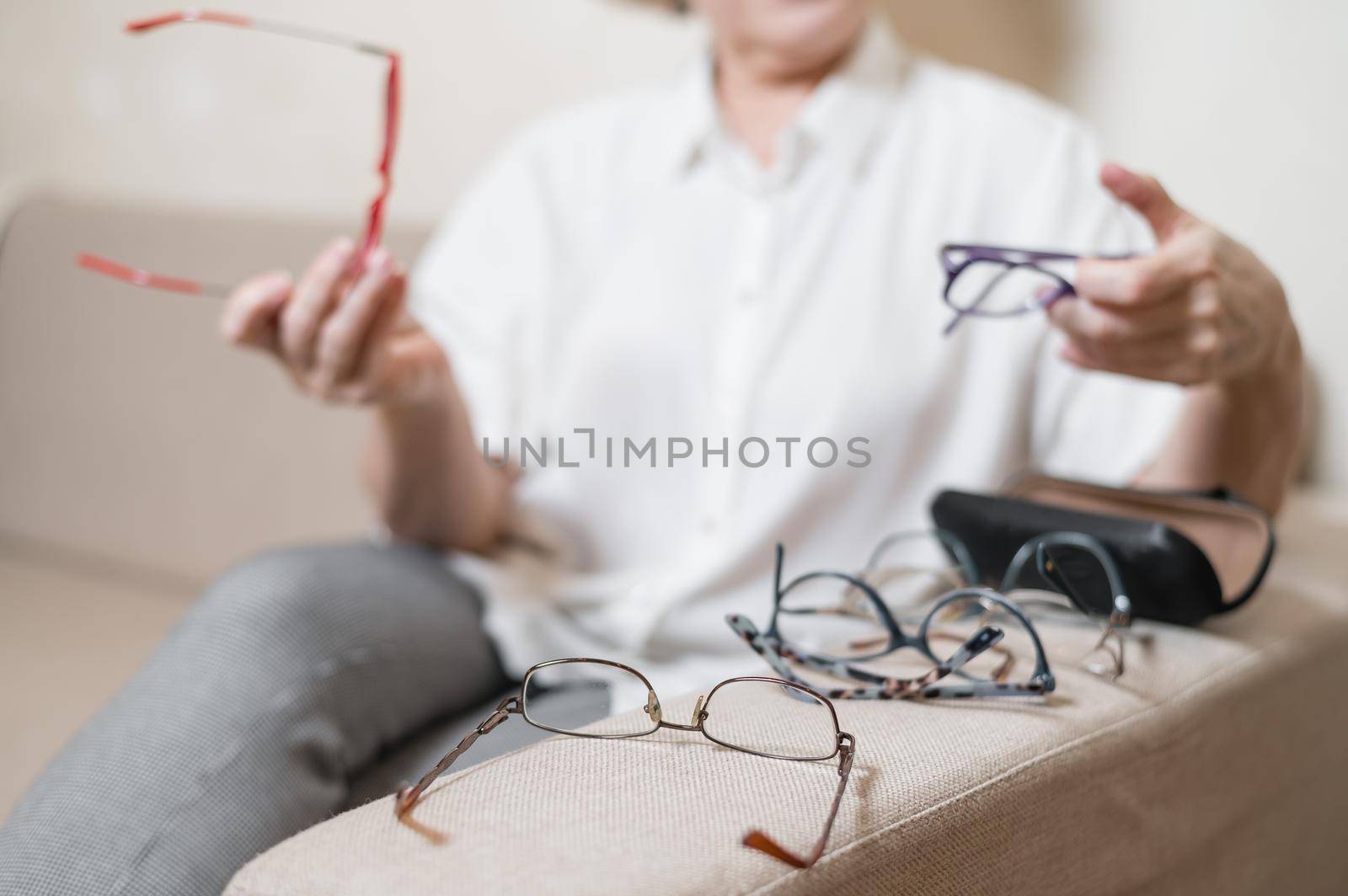 An elderly Caucasian woman chooses glasses from her home collection by mrwed54