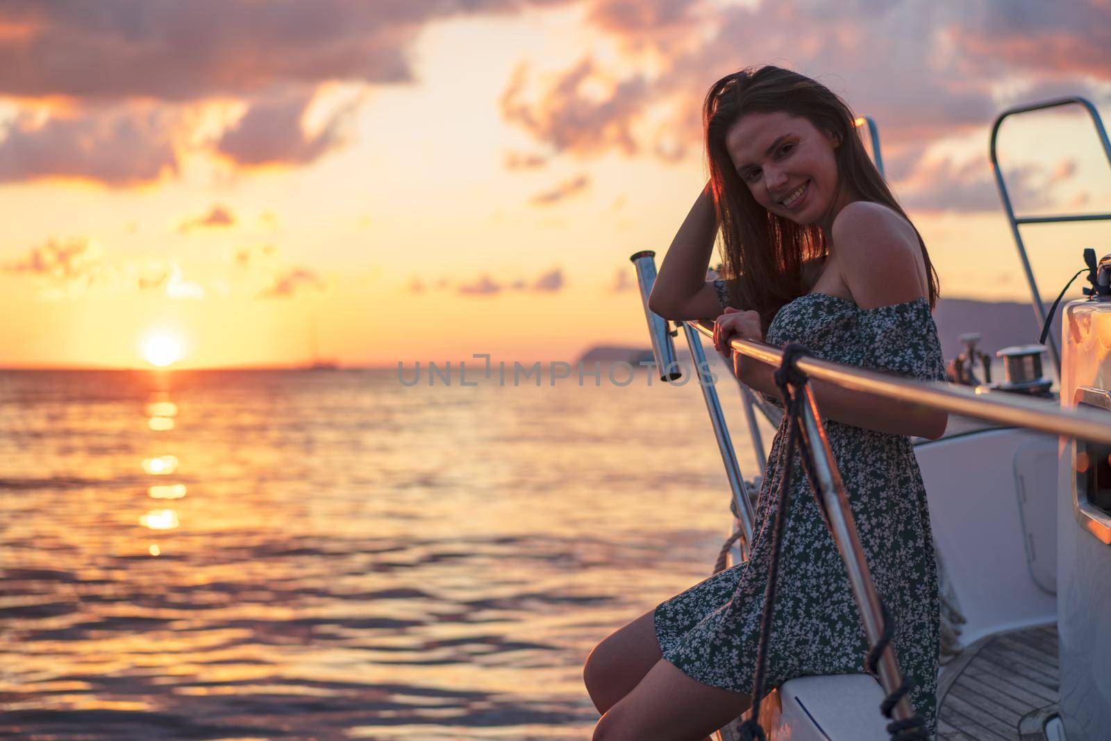 Young attractive woman sitting on the deck of the yacht and enjoying sunset