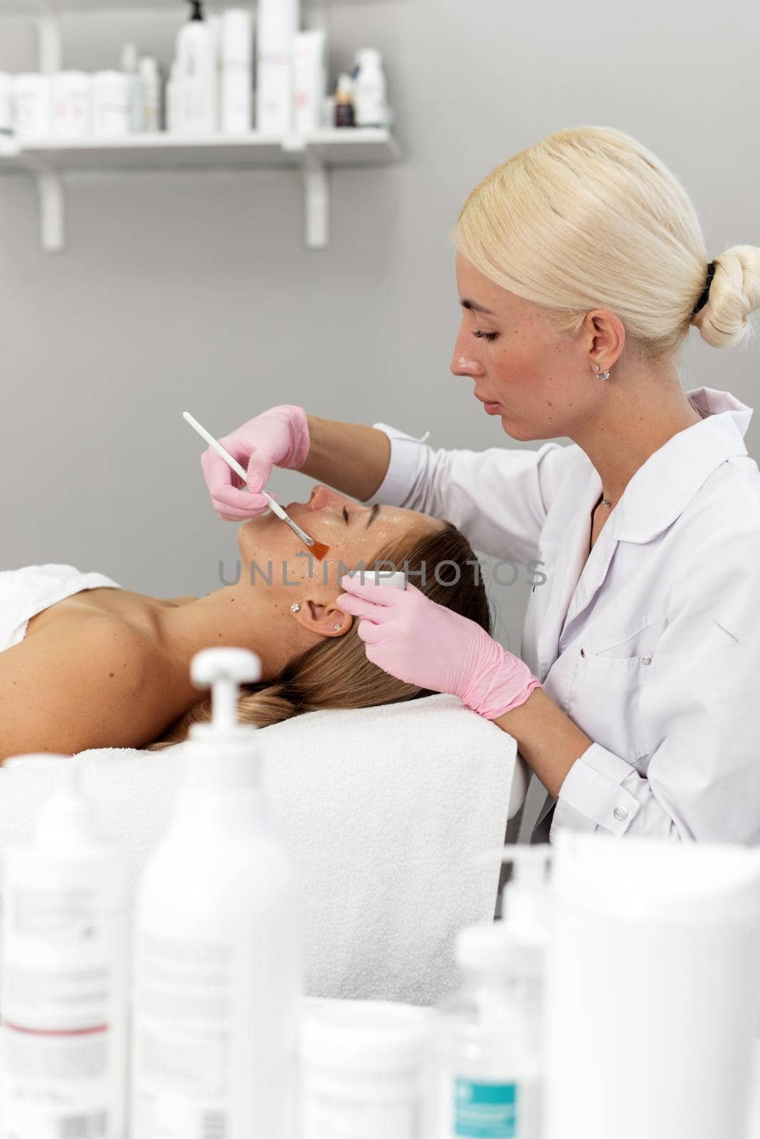 A woman does beauty and spa treatments and applies a moisturizer or mask to her face. Cosmetic procedures. Beautician applies clay mask to woman face in spa salon.