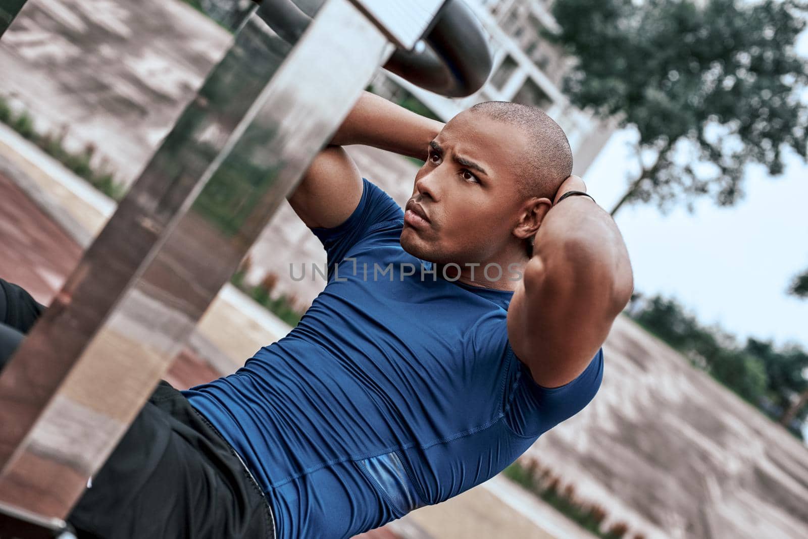 Handsome african man is doing stretching exercises at open air gym near the park. He uses exercises for his abdomen