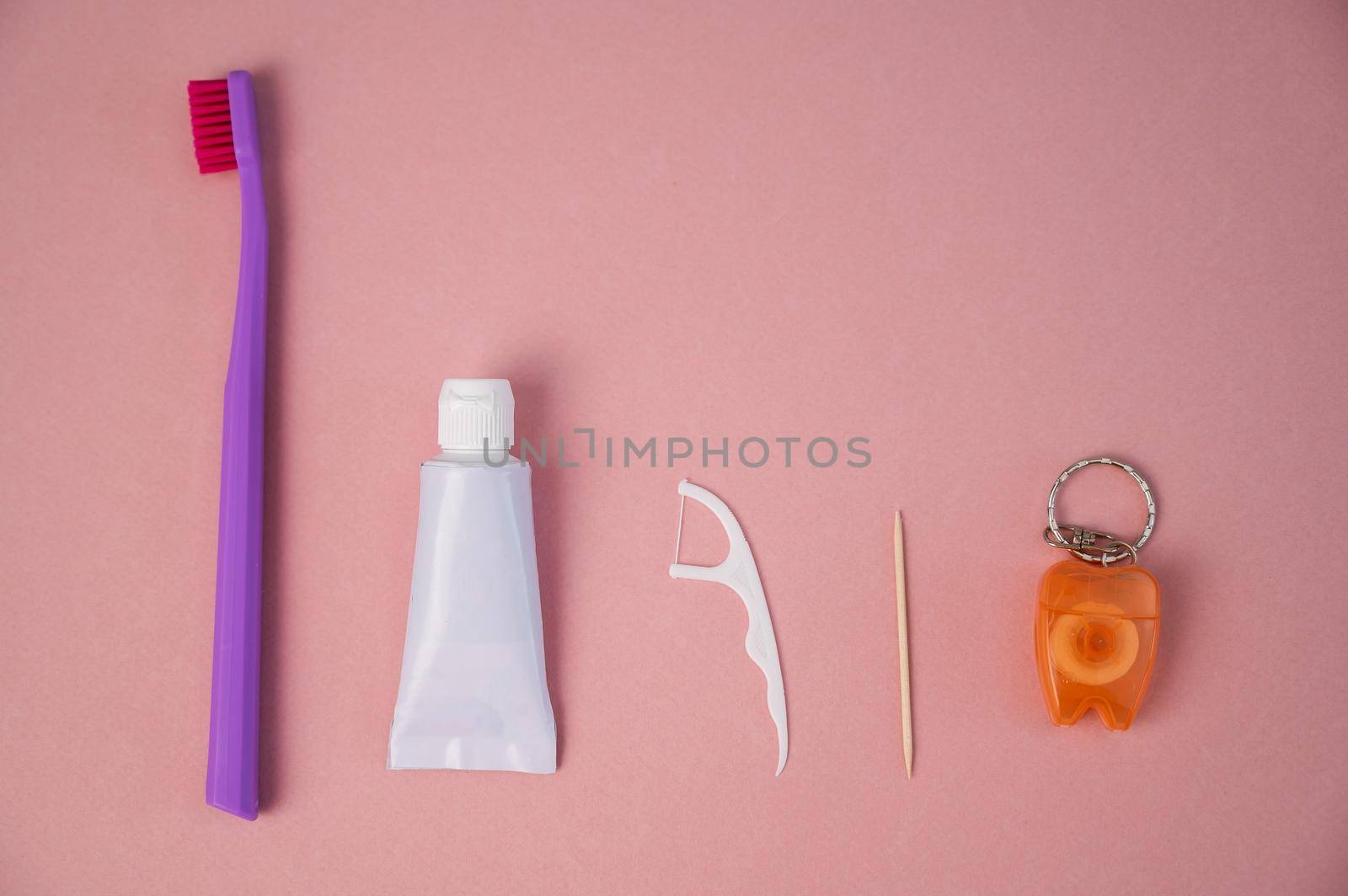 Personal oral hygiene product on a pink background. Toothbrush tube toothpaste toothpick and floss. Flat lay by mrwed54