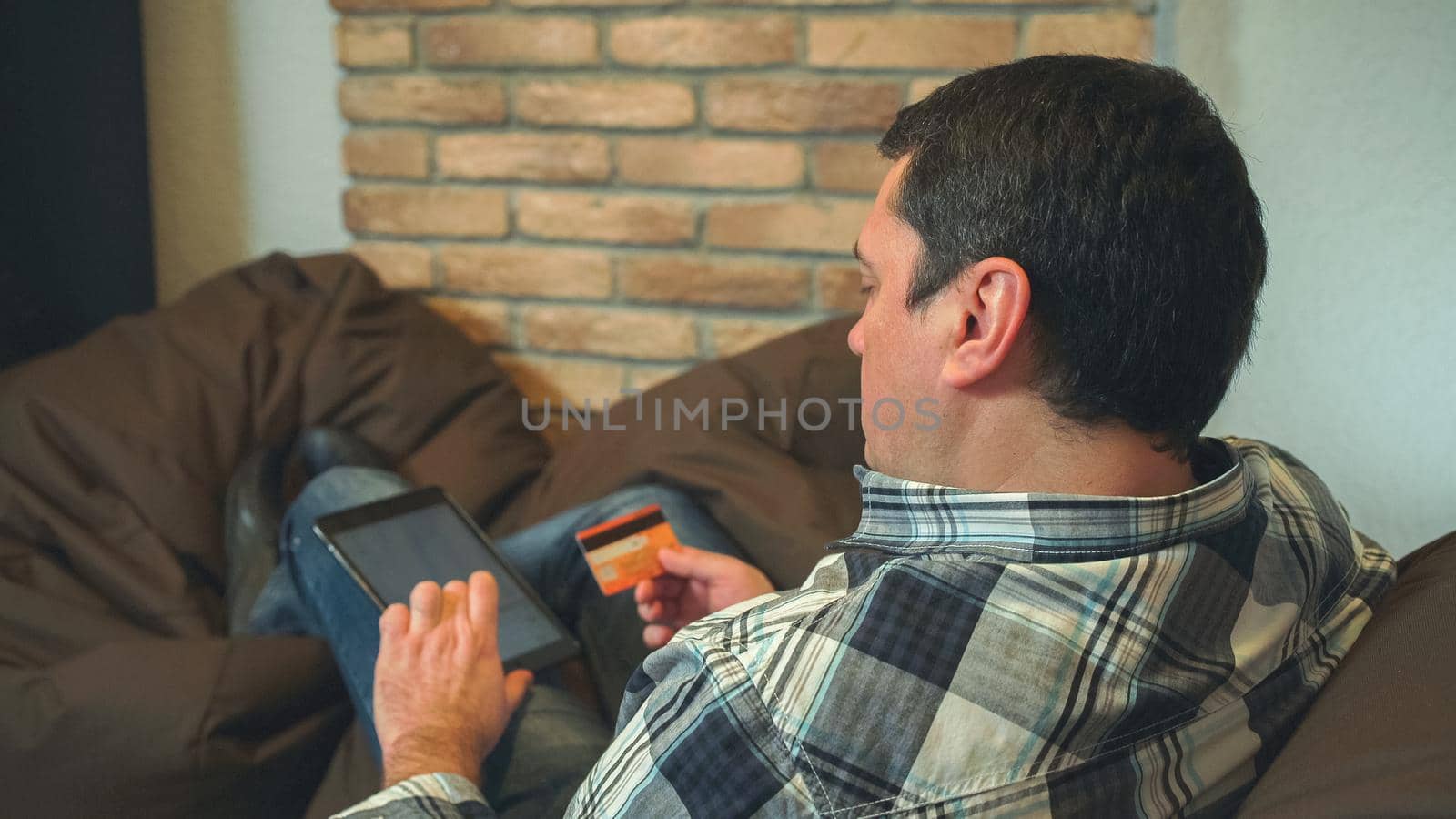 the man lie on the sofa and buy online. He holds in hands digital tablet and credit card