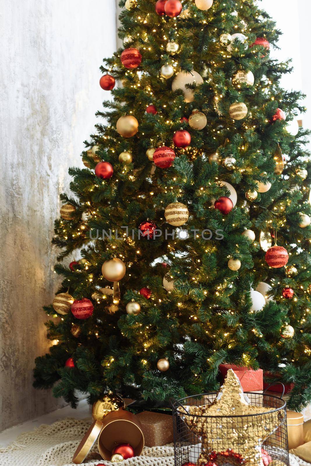 Christmas tree with red and gold balls and gold garland lights in a bright room