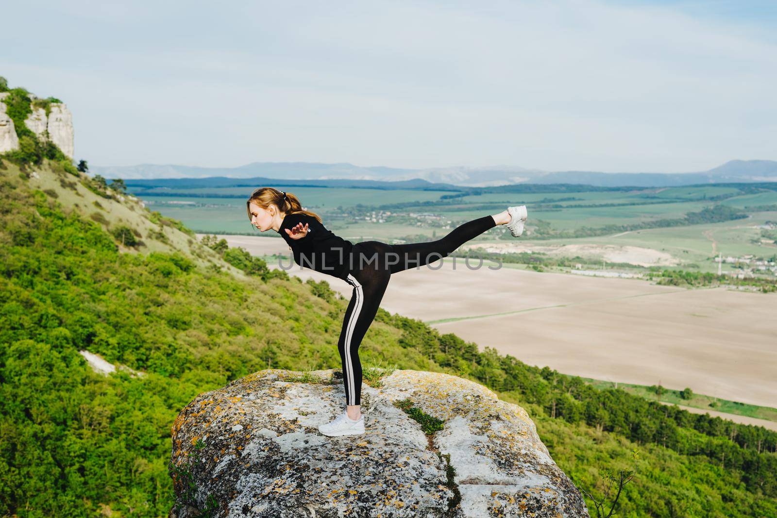 A girl in a swallow pose on the edge of a cliff. Outdoor sports.
