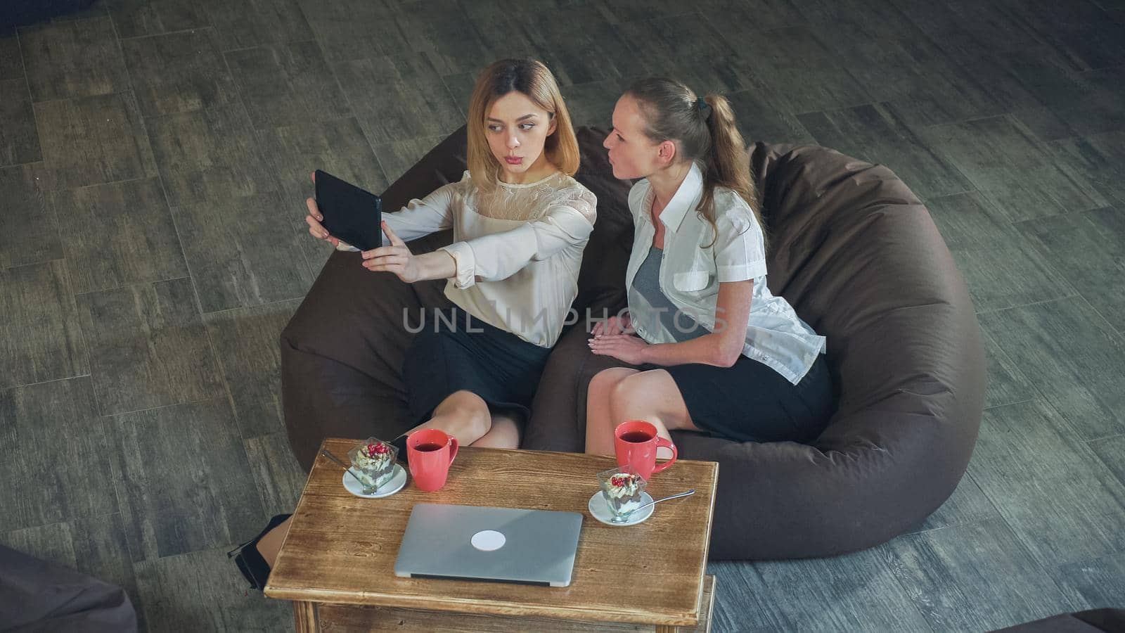 Two women take selfie in the cafe by digital tablet. On the table cups and laptop
