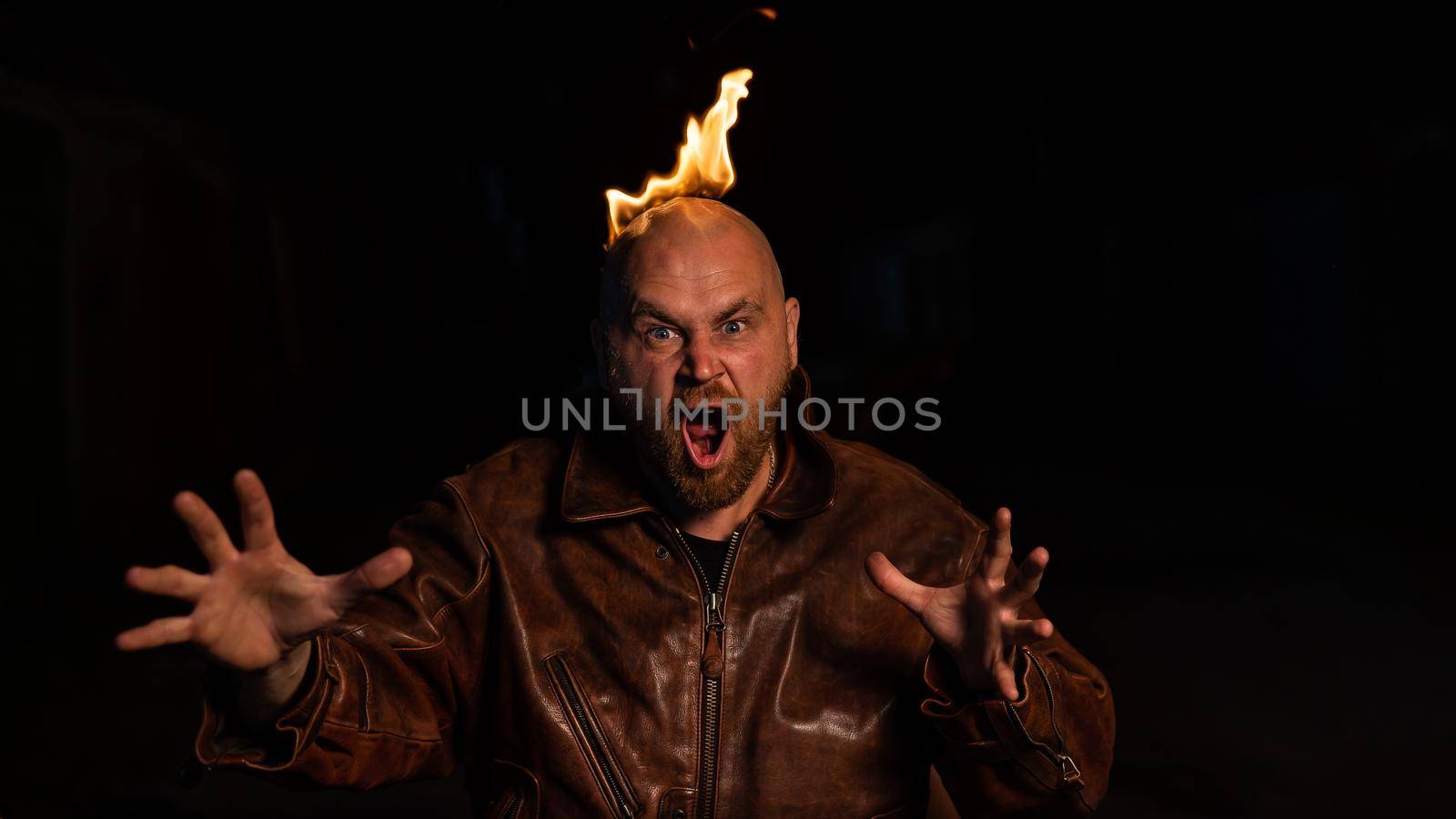 Bald man in a leather jacket with a burning head on a dark background