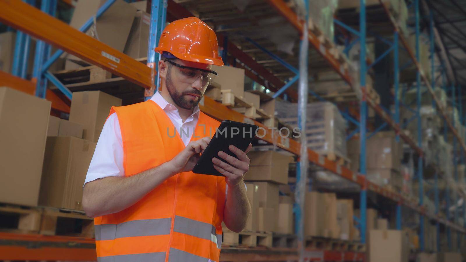 Manager at warehouse using digital touch screen tablet. Handsome worker entering data. Adult man at work in storehouse.