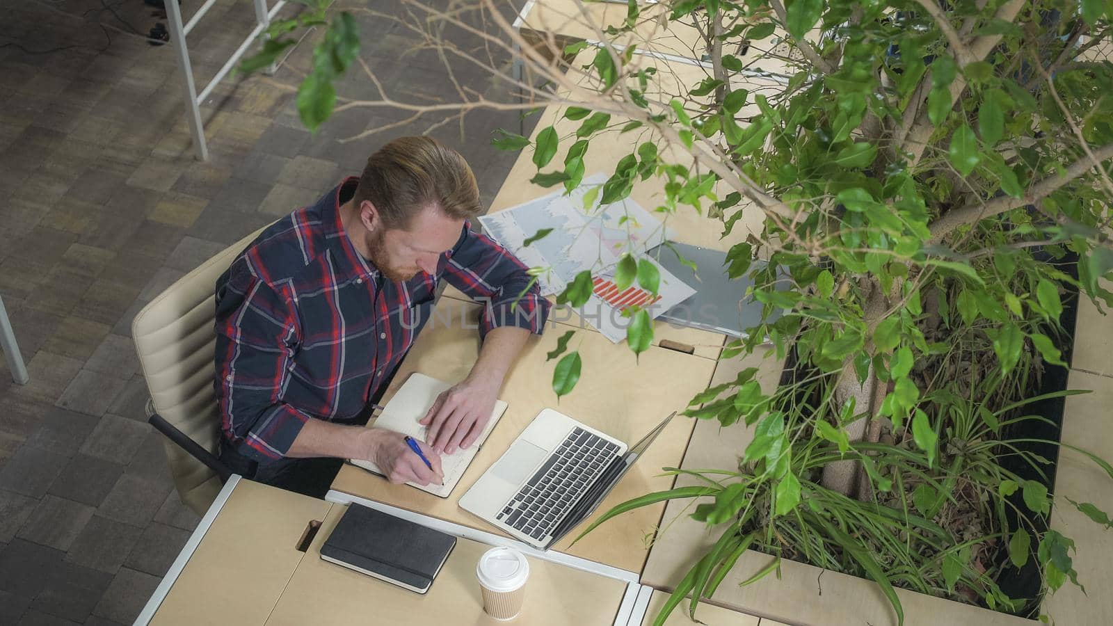 Bearded man working at a computer and taking notes on a pad. Soft panorama