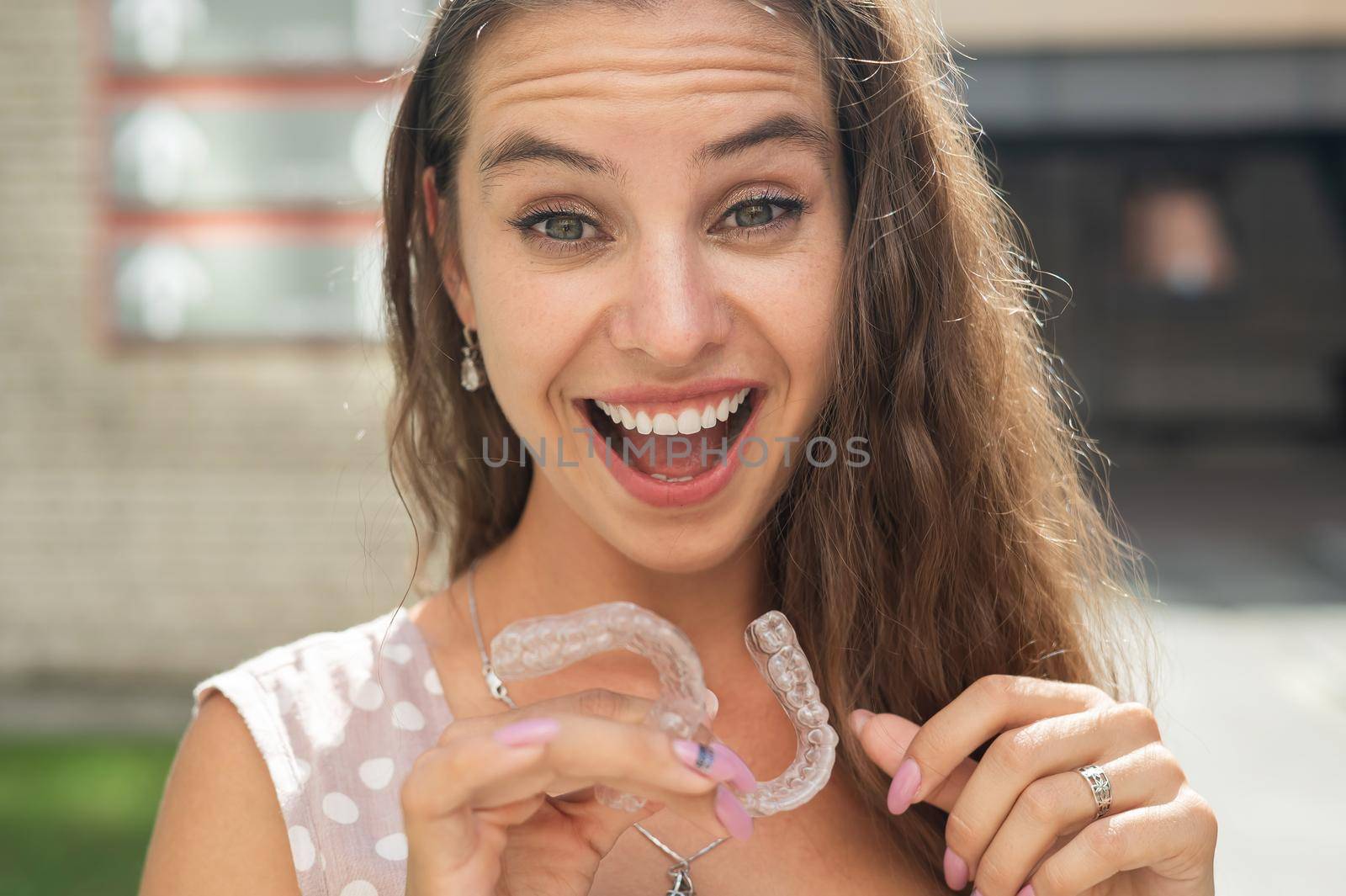 Beautiful caucasian woman holding transparent mouth guards for bite correction. Girl with silicone braces outdoors. by mrwed54