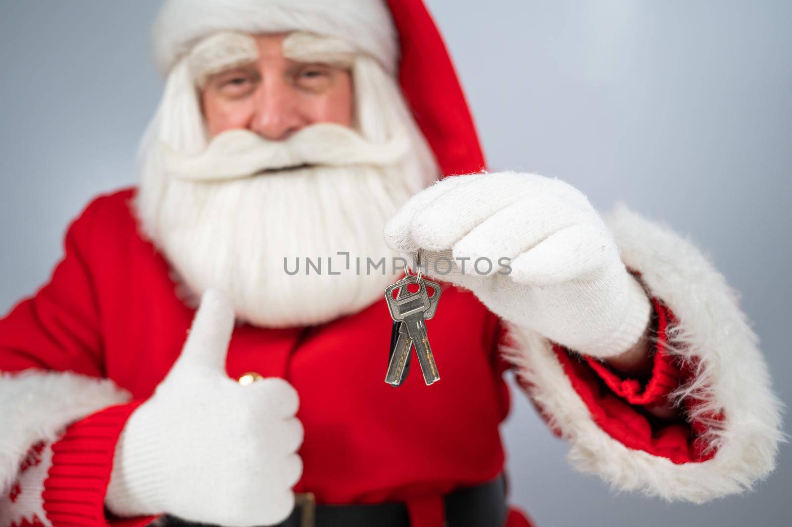 Santa Claus holds keys on a white background and thumb up. New home gift for christmas