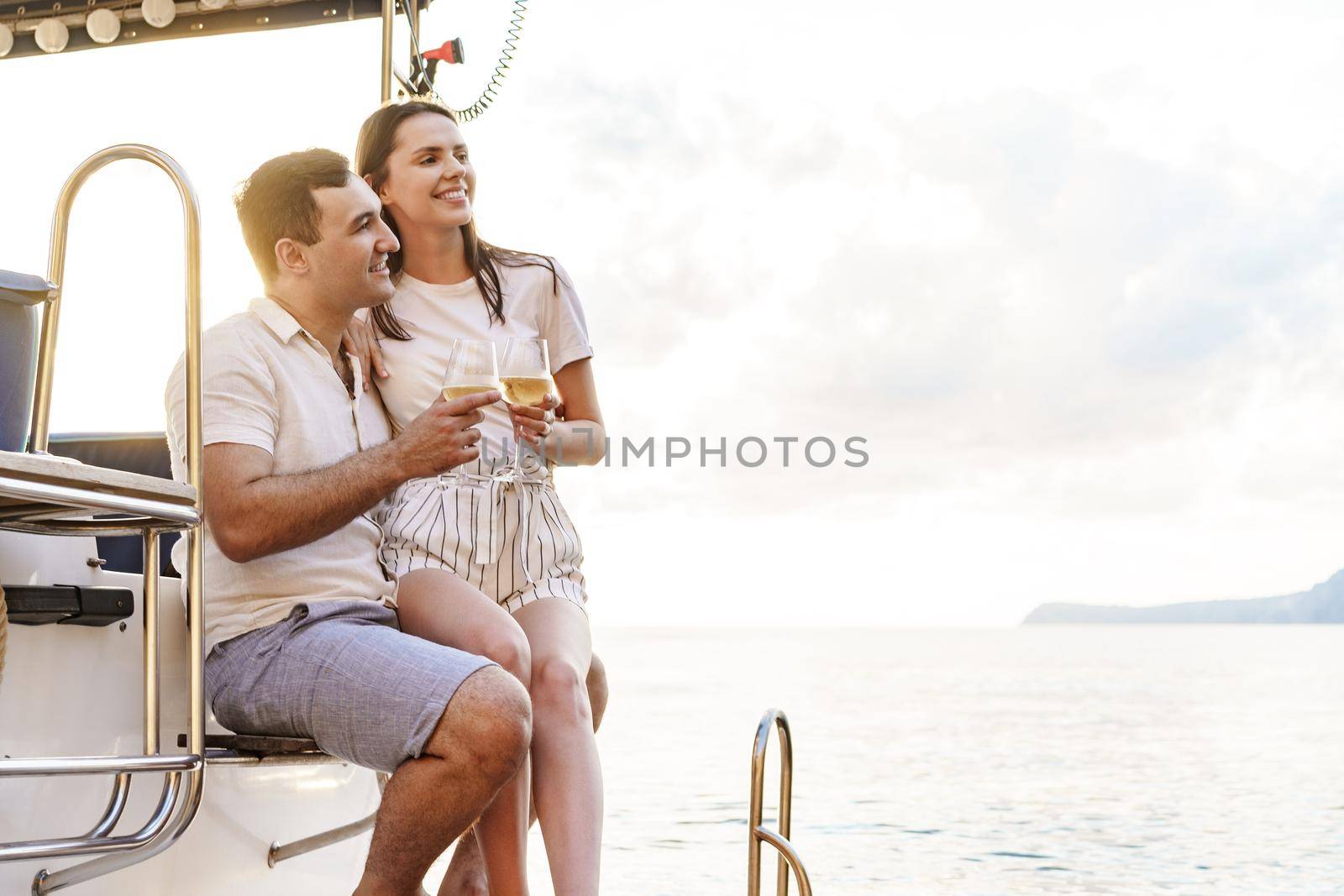 Young loving couple sitting on the yacht deck and drinking wine together