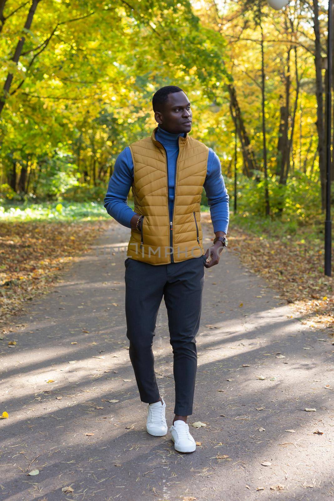 Cheerful african american young man in stylish clothes walks in autumn park on sunny warm autumn day. Concept of weekend and outdoor recreation by Satura86