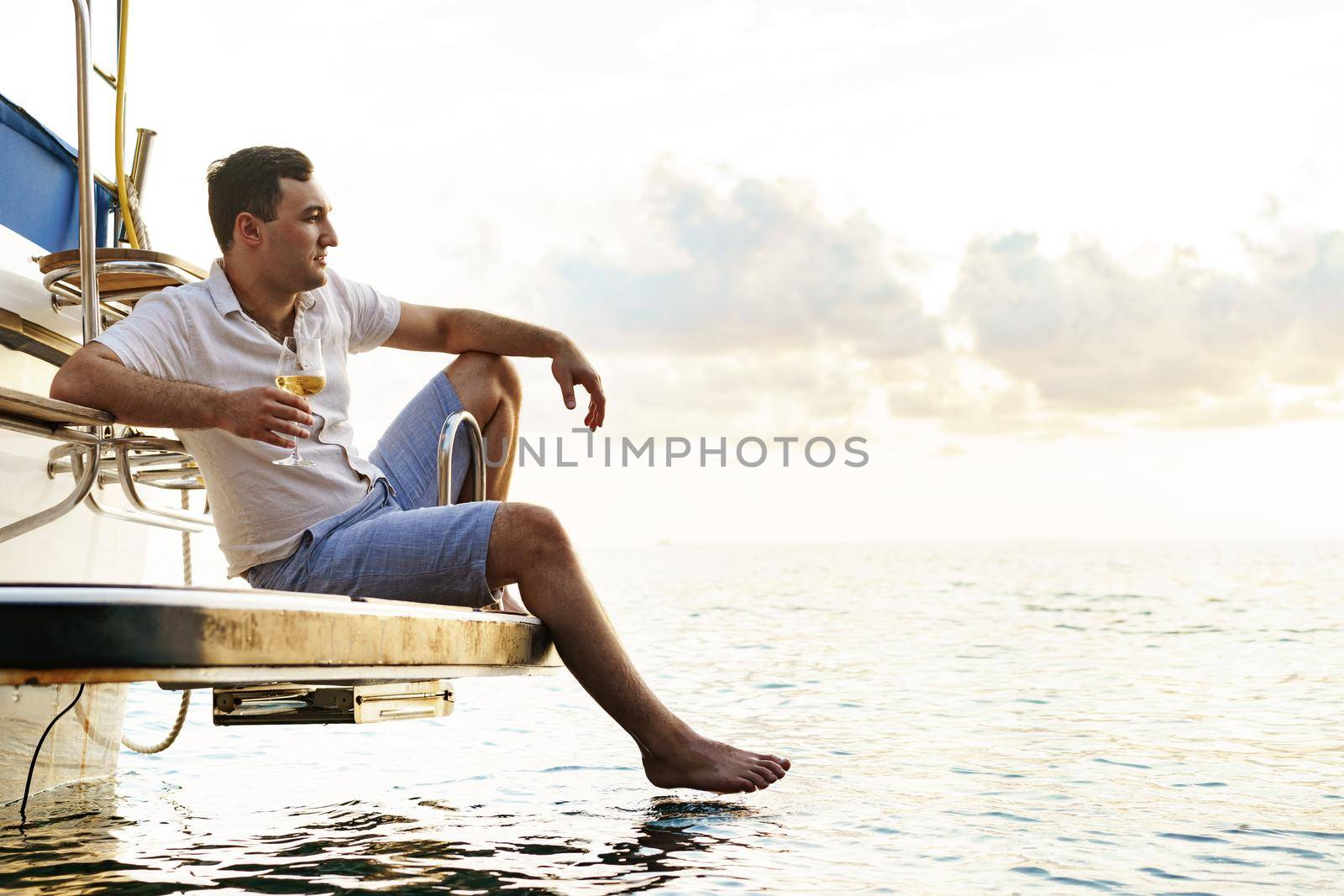 Young man holding a glass of wine on an open deck of a cruise boat, close up