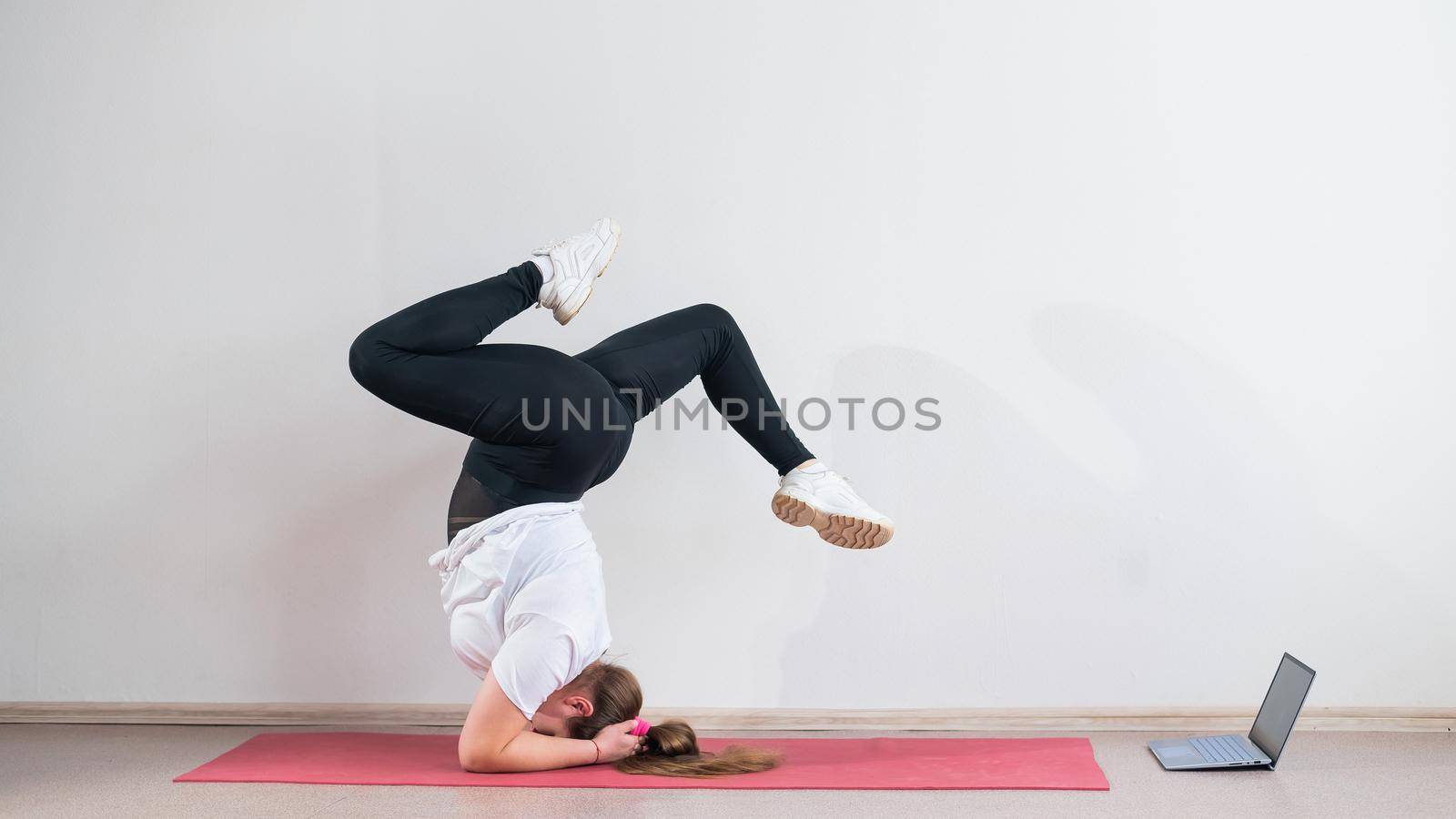 A chubby young woman watches an online yoga lesson on a laptop. Distance sports training. Forearm stand.