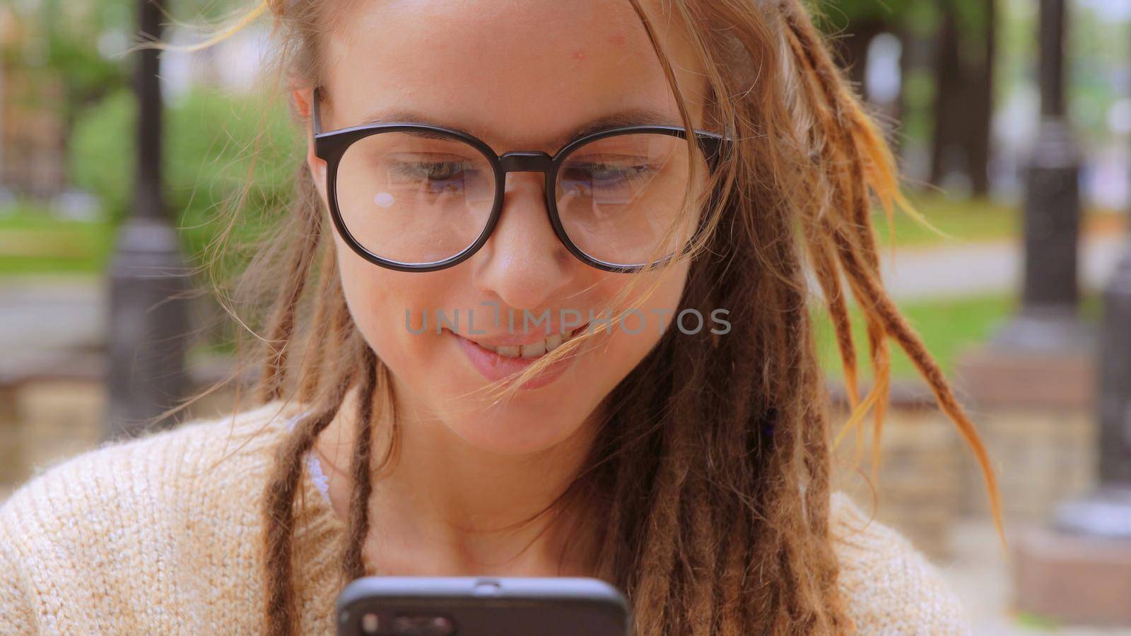 close up face young caucasian woman with dreadlocks and eyeglasses using smartphone texting message or chatting online