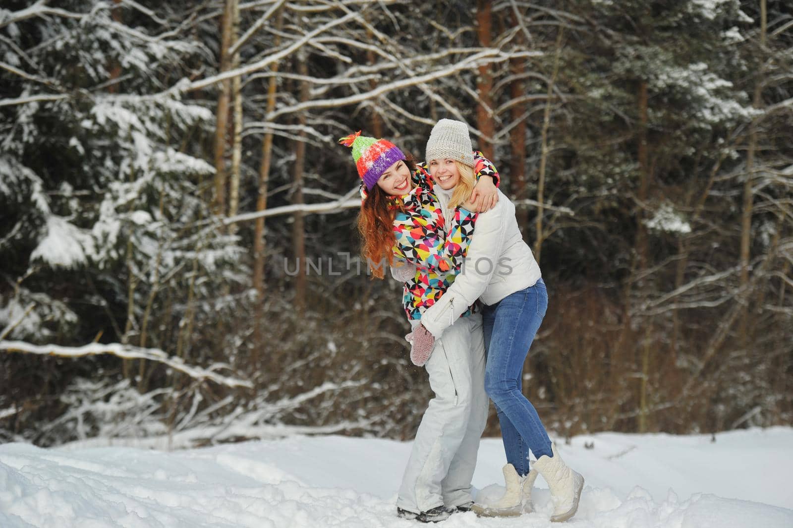 Two girls in the winter forest emotionally hug and smile.Happy women hug and Express joy.