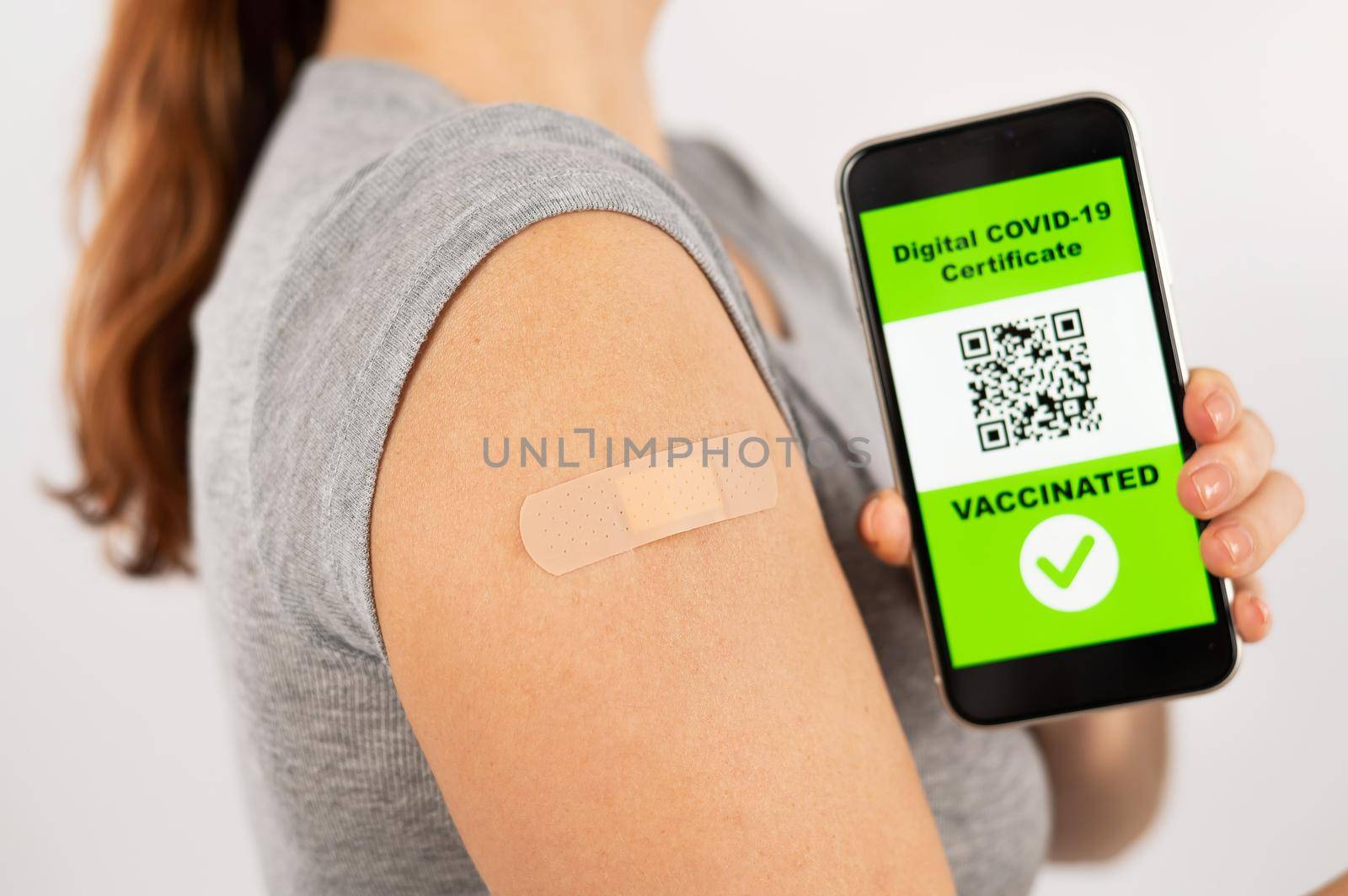 Woman with a plaster on her shoulder after vaccination and demonstrates the QR code on a smartphone. by mrwed54