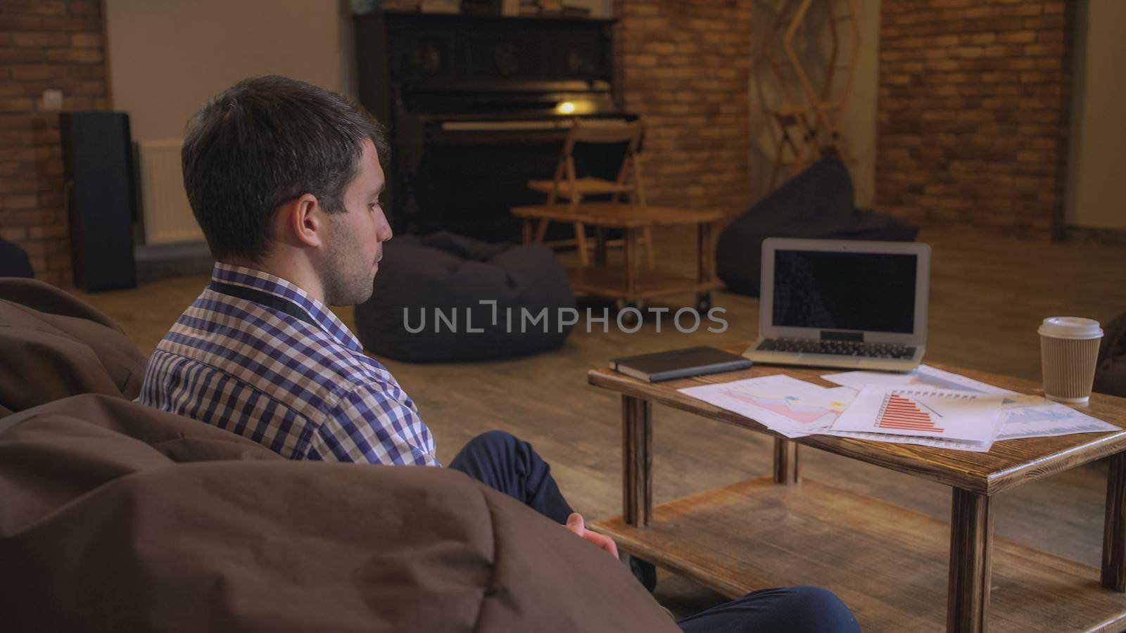 Attractive man sitting on the couch waiting for a meeting with a partner. On the table laid out charts and tables, next to a laptop lies diary.