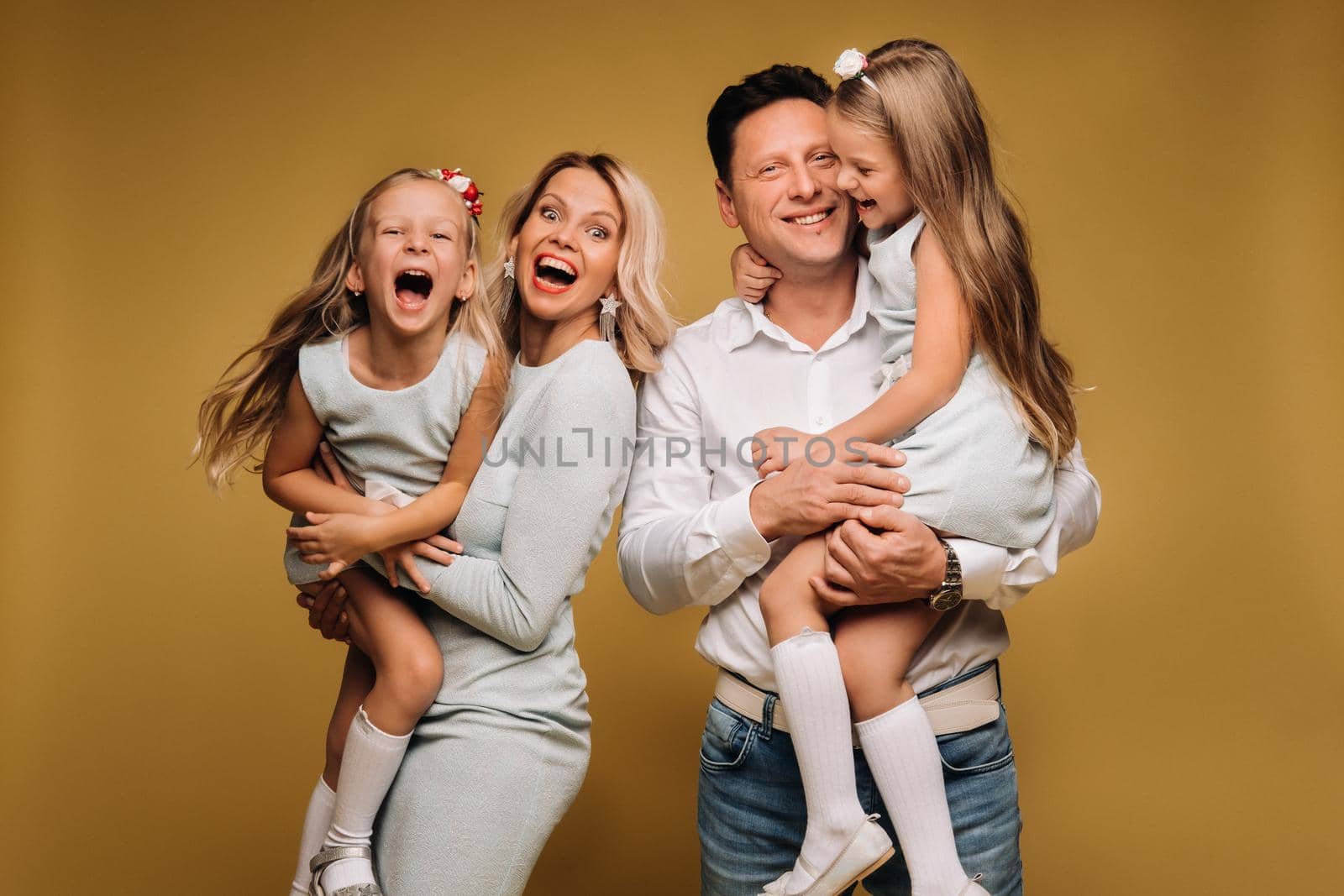 Happy parents hold their children in their arms and smile on a yellow background. an emotional family of four.