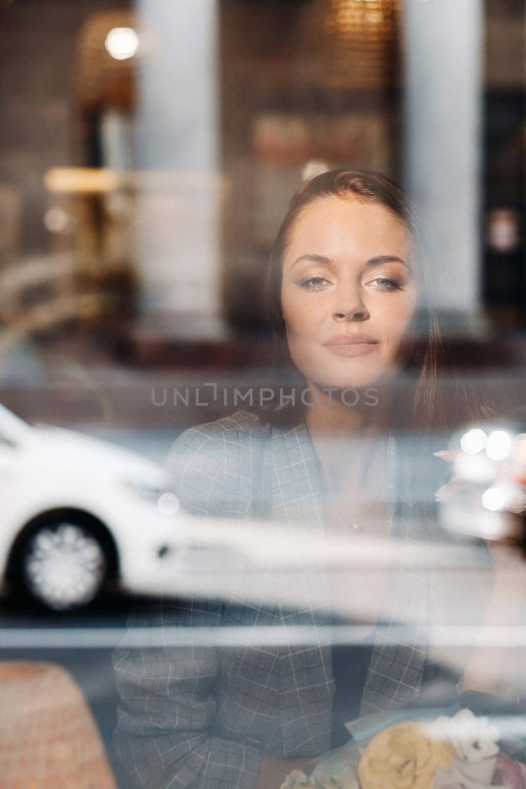Portrait of a young European girl with long hair in a cafe sitting near the window, a tall girl in a jacket with long hair in the reflection of the window in a cafe.
