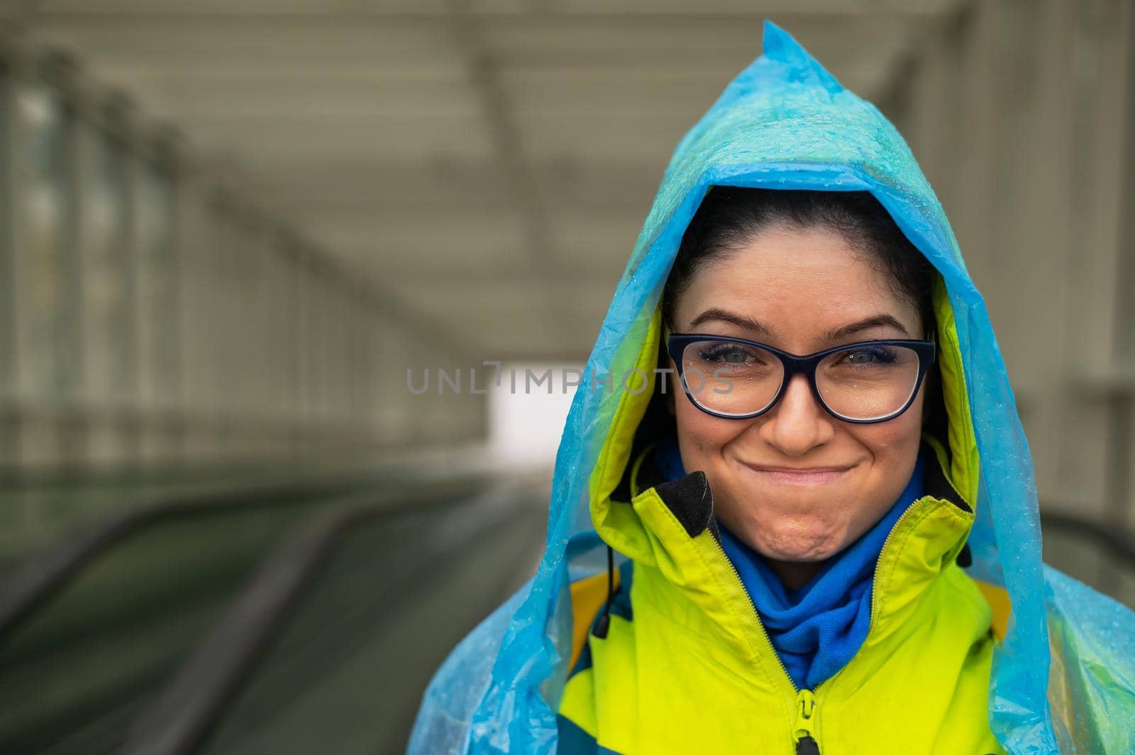 Smiling young woman in a jacket and raincoat on a travolator. Girl in protective clothing from the rain by mrwed54