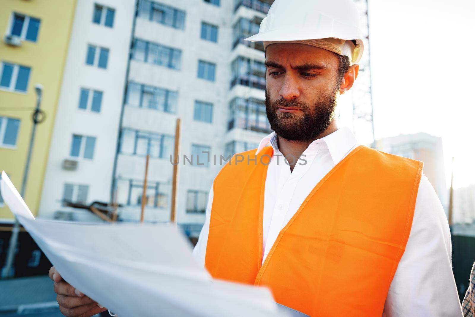 Builder or architect in hardhat supervising a project, looking at blueprints, close up